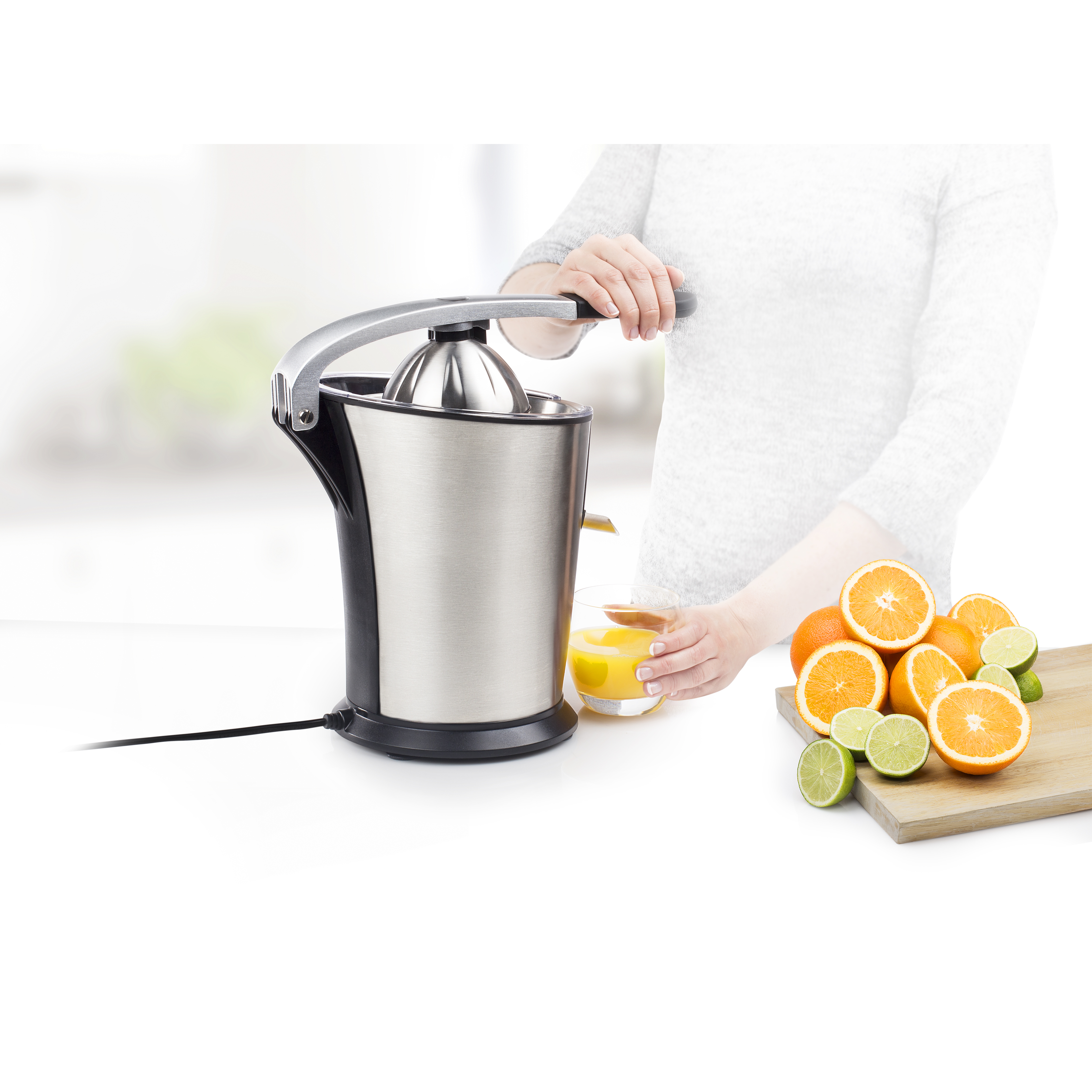 Een vrouw perst sinaasappelsap met een citruspers, omringd door sinaasappels en limoenen.