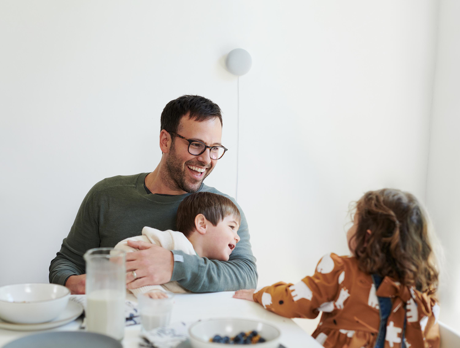Man met kinderen aan een tafel. Lachend, een lamp aan de muur.