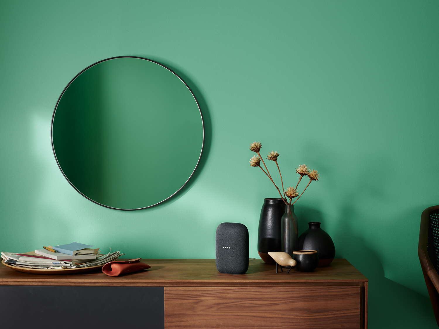 Interieur met slimme speaker, spiegel en houten console tegen een groene muur.