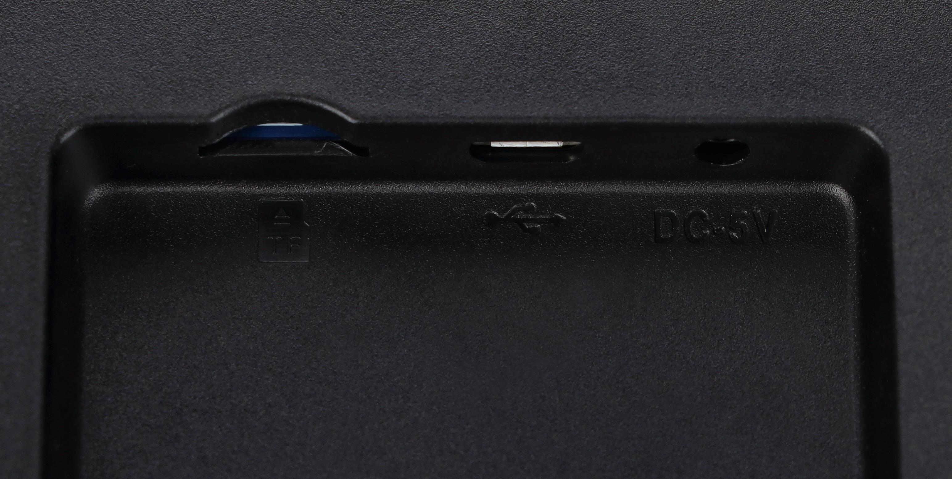 Nahaufnahme zeigt Anschlüsse: SD-Karte, USB und DC 5V auf einem schwarzen Gerät. Die Oberfläche ist strukturiert.