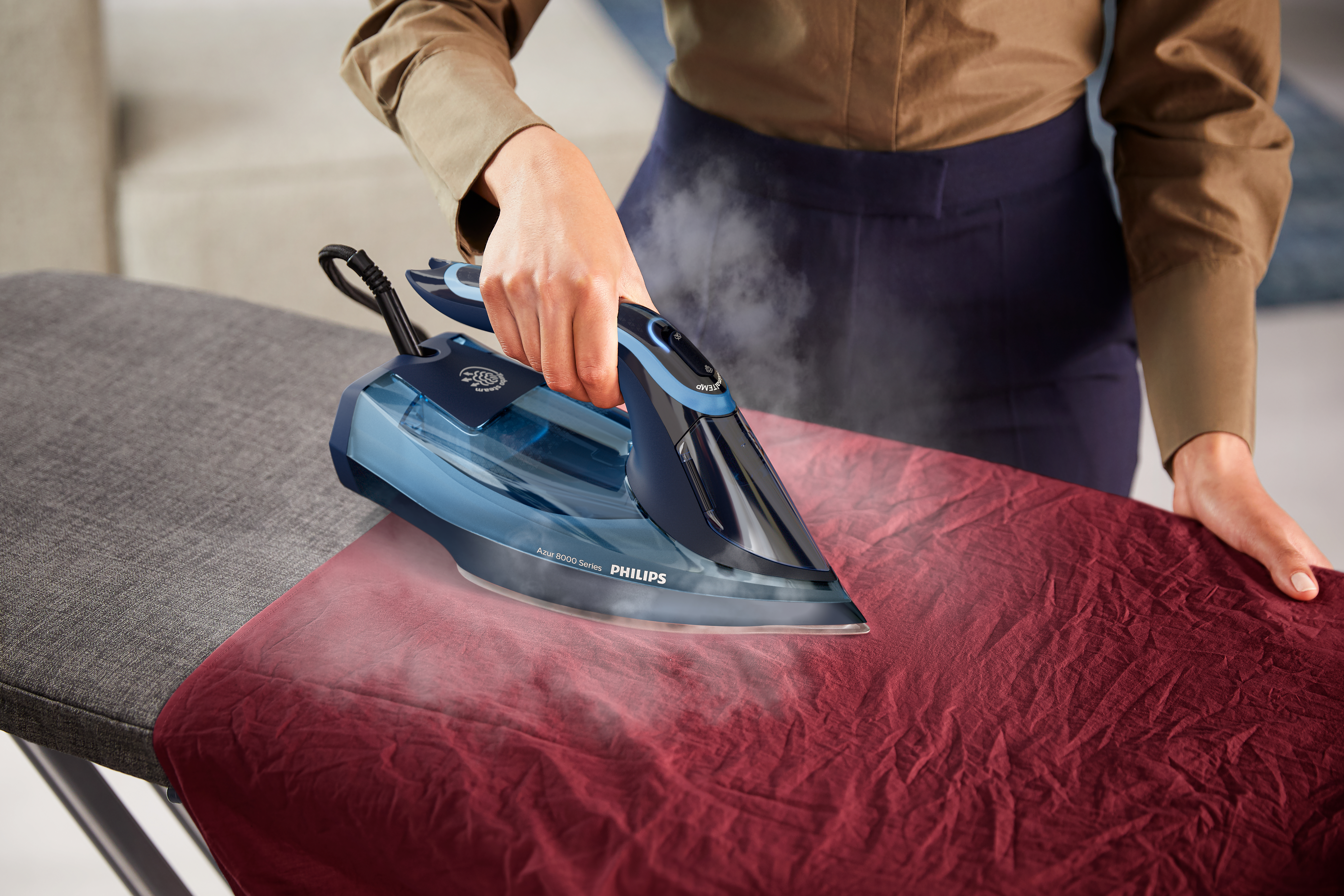 Una plancha azul planchando tela roja en una tabla de planchar.