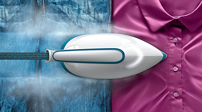 Una plancha vaporizando vaqueros y una camisa rosa. Sale vapor de la plancha.