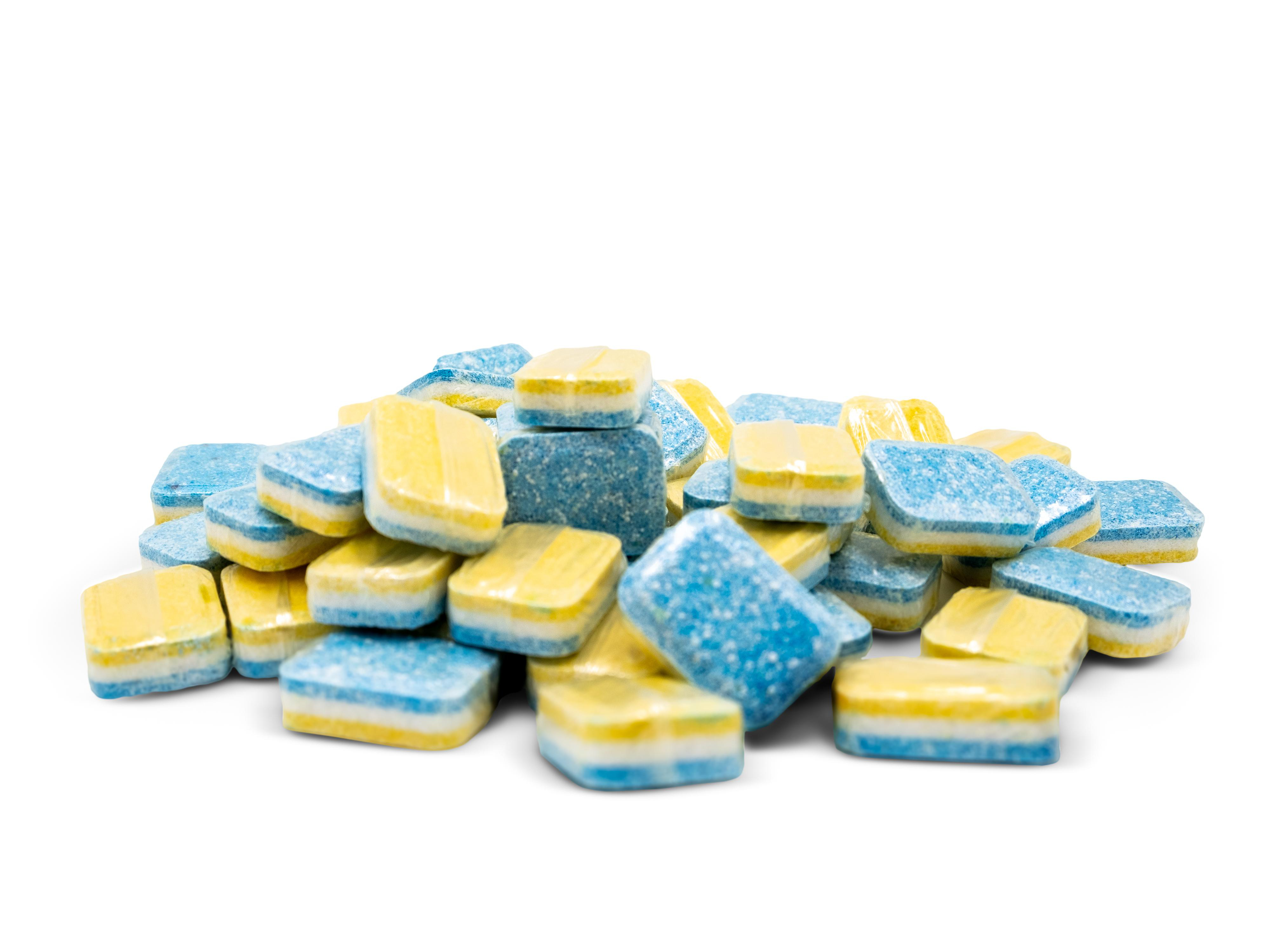 Ein Haufen gelber und blauer quadratischer Reinigungstabletten auf einer weißen Oberfläche.