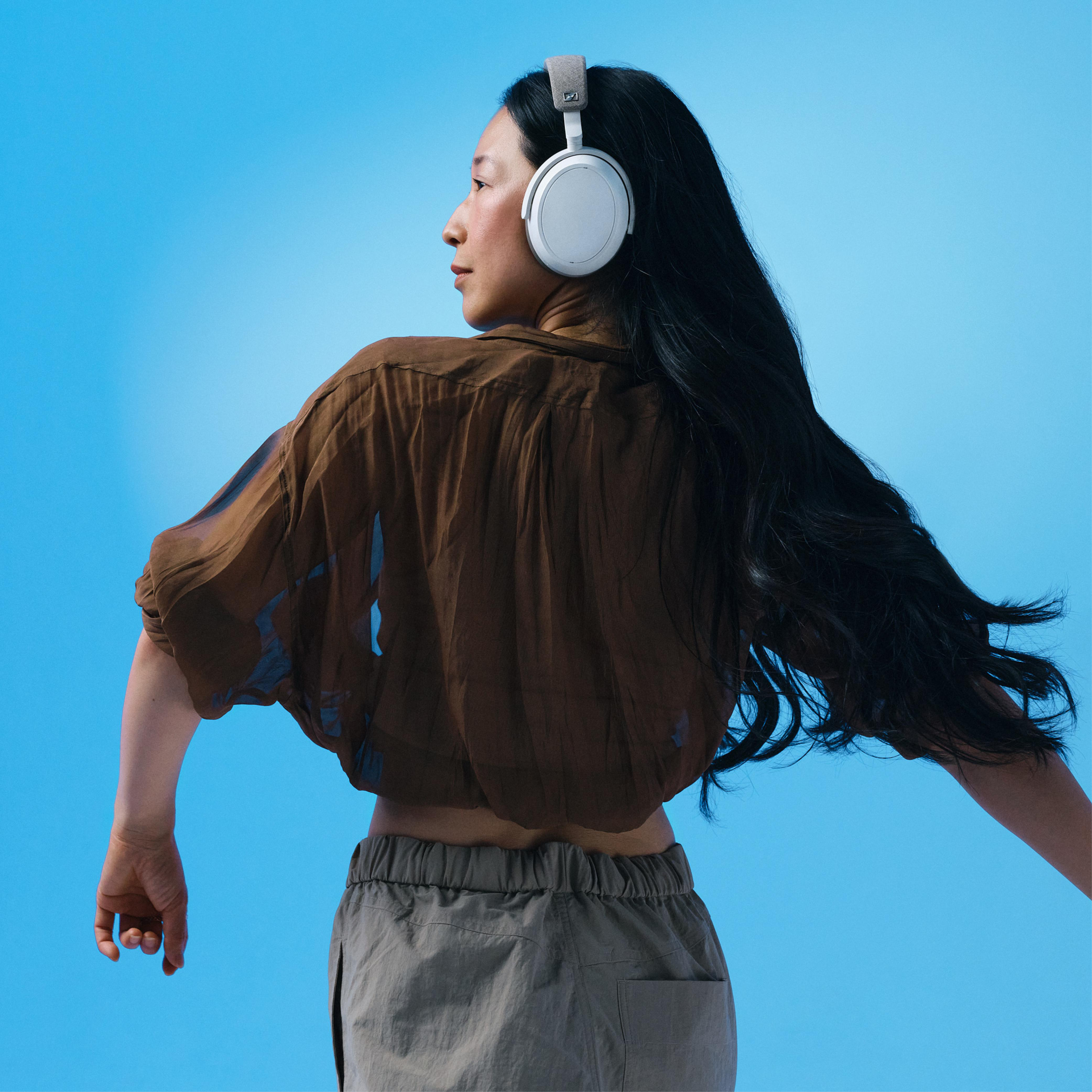 Eine Frau mit weißen Kopfhörern. Sie schaut über ihre Schulter, vor blauem Hintergrund.