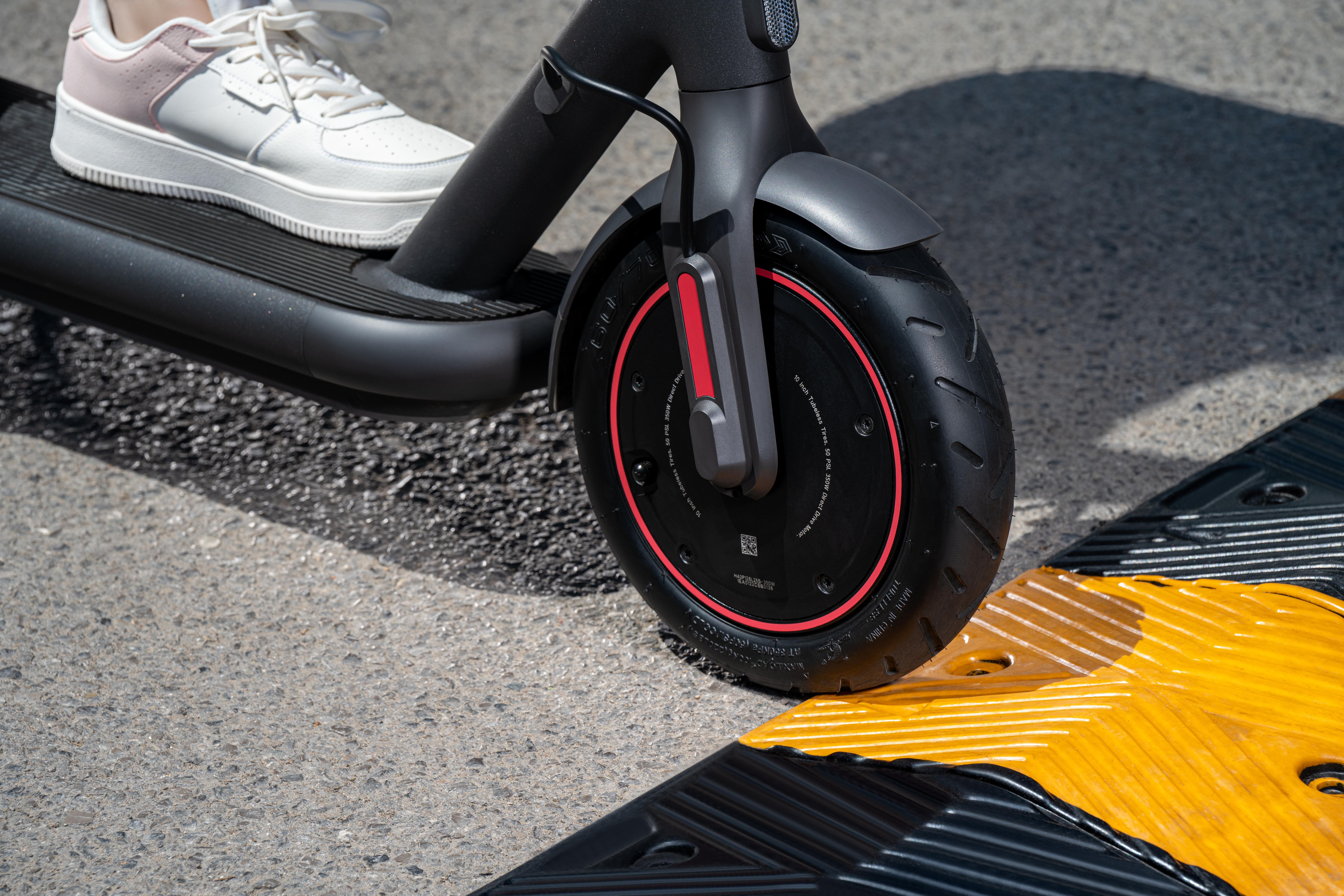 Der Fuß einer Person auf einem Elektroroller, der über eine Bodenwelle auf einer Asphaltstraße fährt.