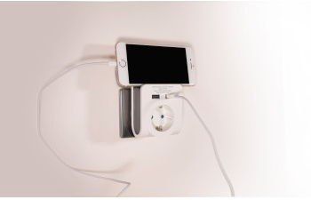 A white phone charging via a wall outlet, connected to a charging station with a USB port.