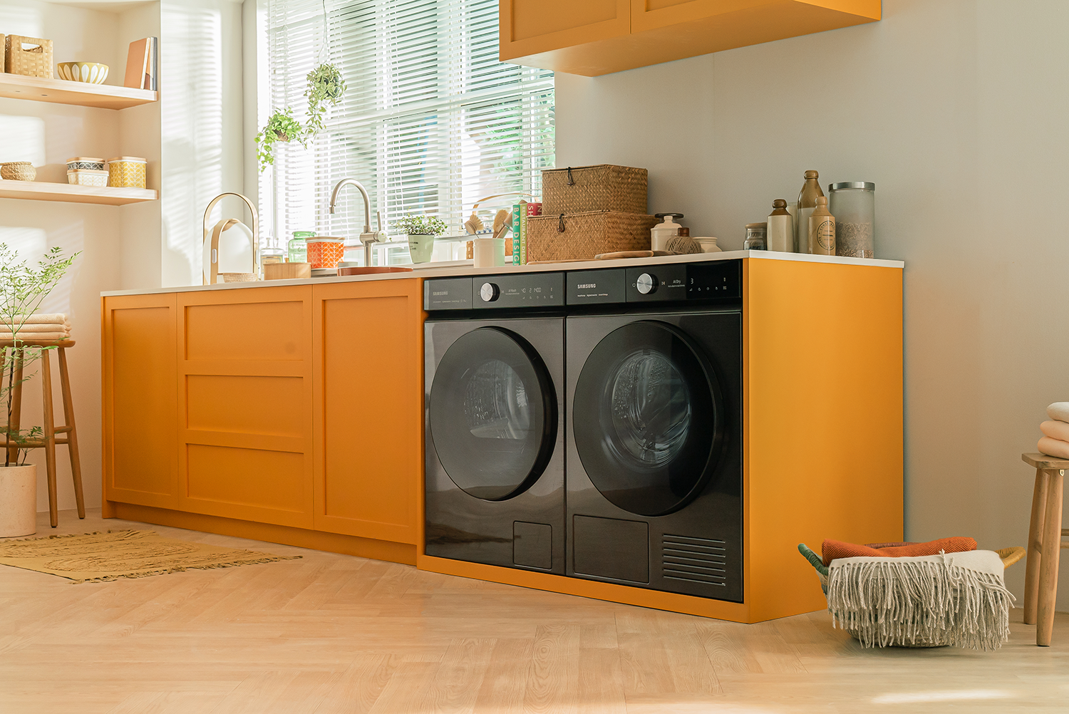 Wasruimte met oranje kasten, zwarte wasmachine/droger en een raam. Houten vloer en wit aanrechtblad.