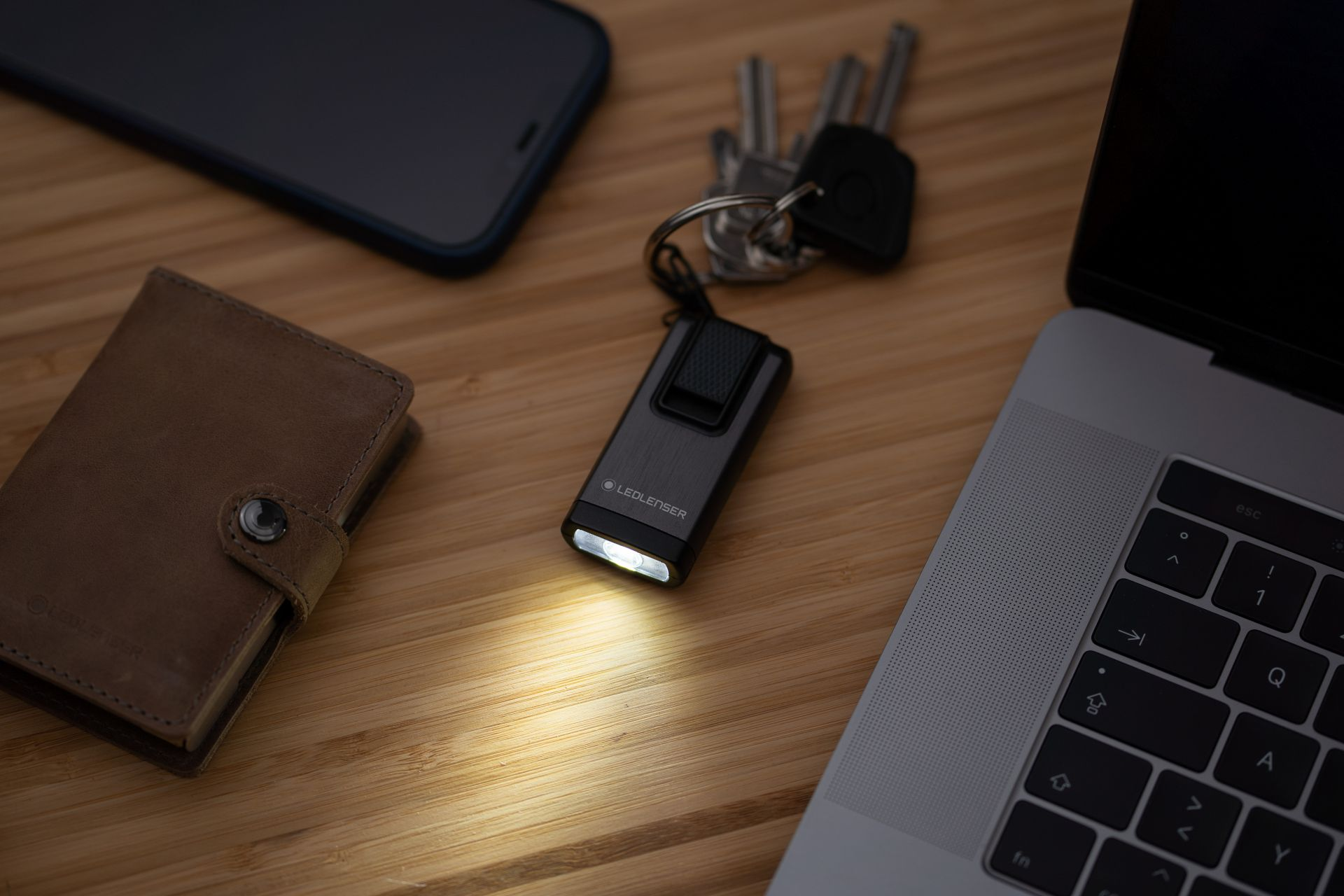 Lampe de poche avec porte-clés, clés, portefeuille et smartphone sur un bureau en bois.