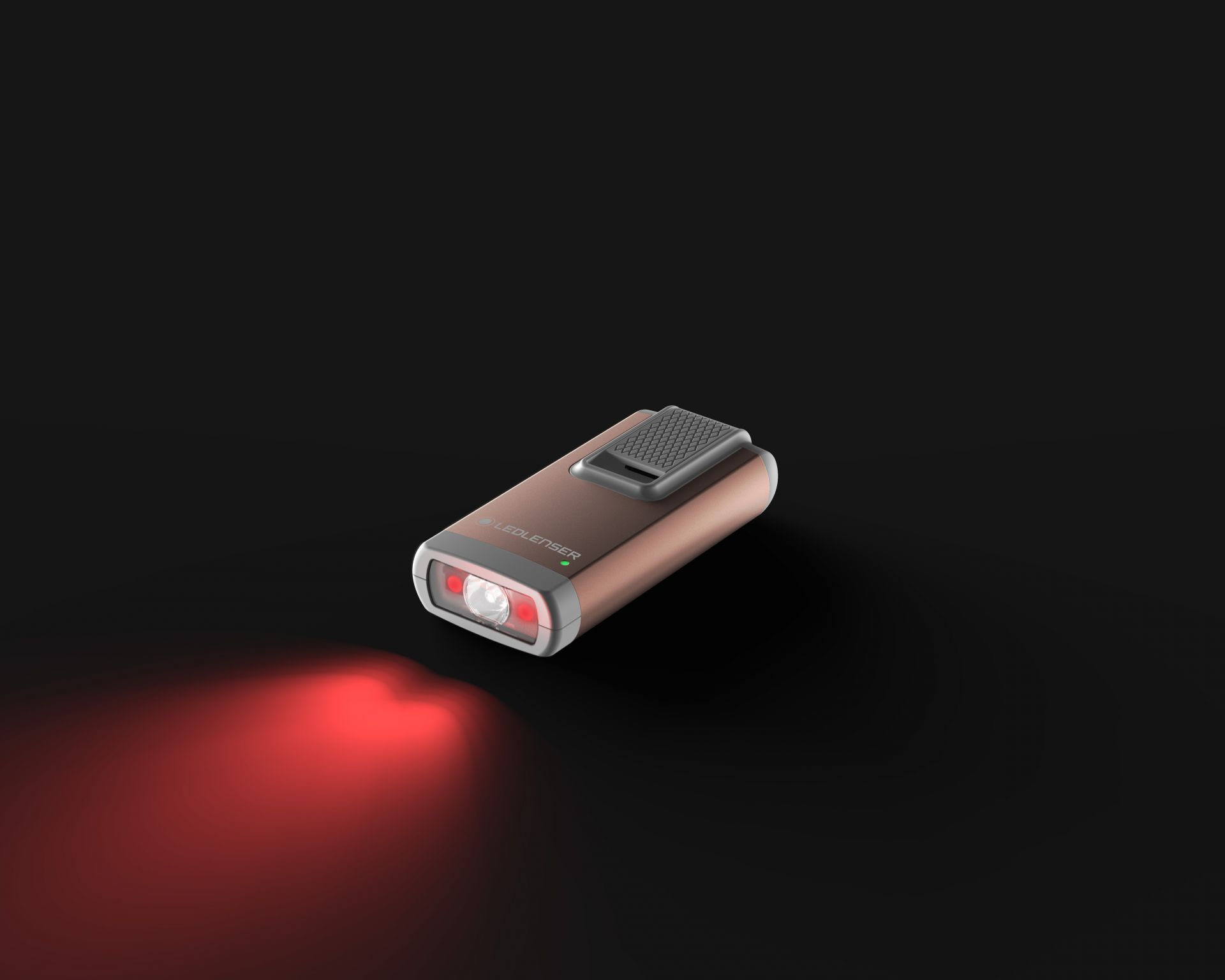 Une lampe de poche cuivrée avec un clip, émettant un faisceau rouge sur une surface sombre.