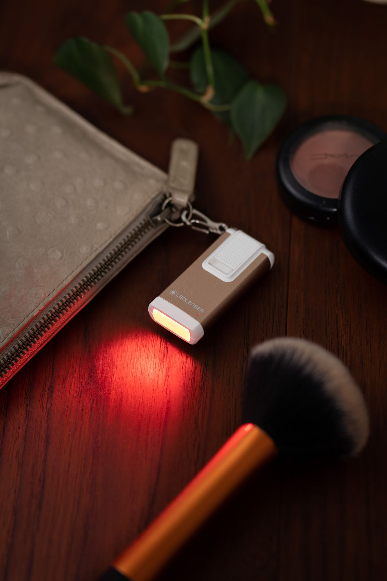 Petite lampe de poche dorée émettant une lumière rouge, à côté de maquillage sur une table.