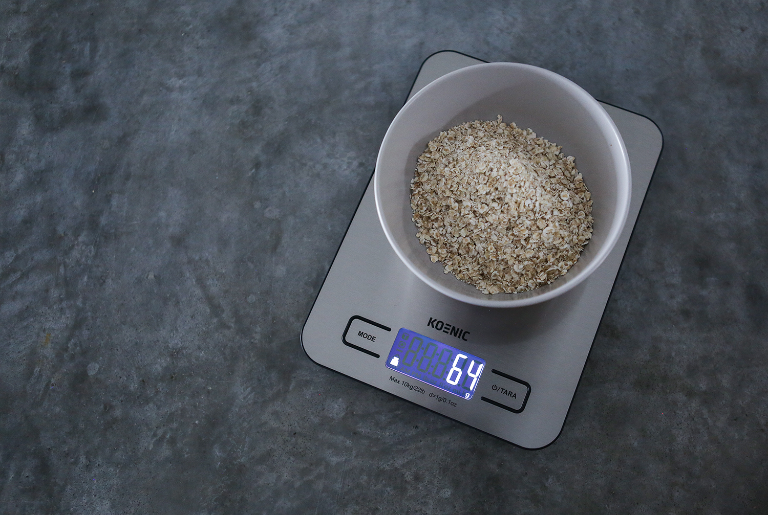 A digital kitchen scale with a bowl of oats on it, displaying the number 64.