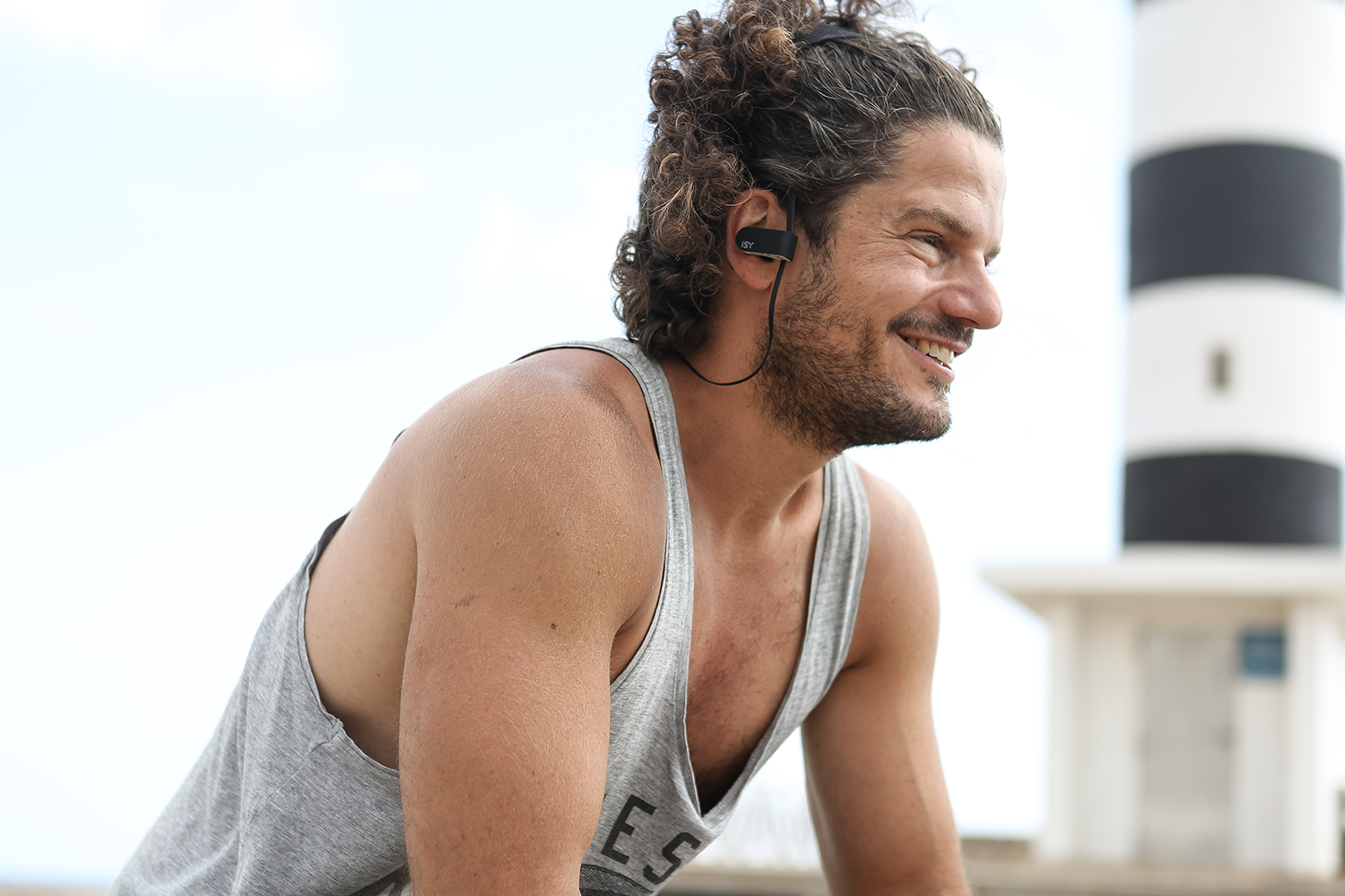 Man wearing headphones smiles. Background includes lighthouse and blue sky.
