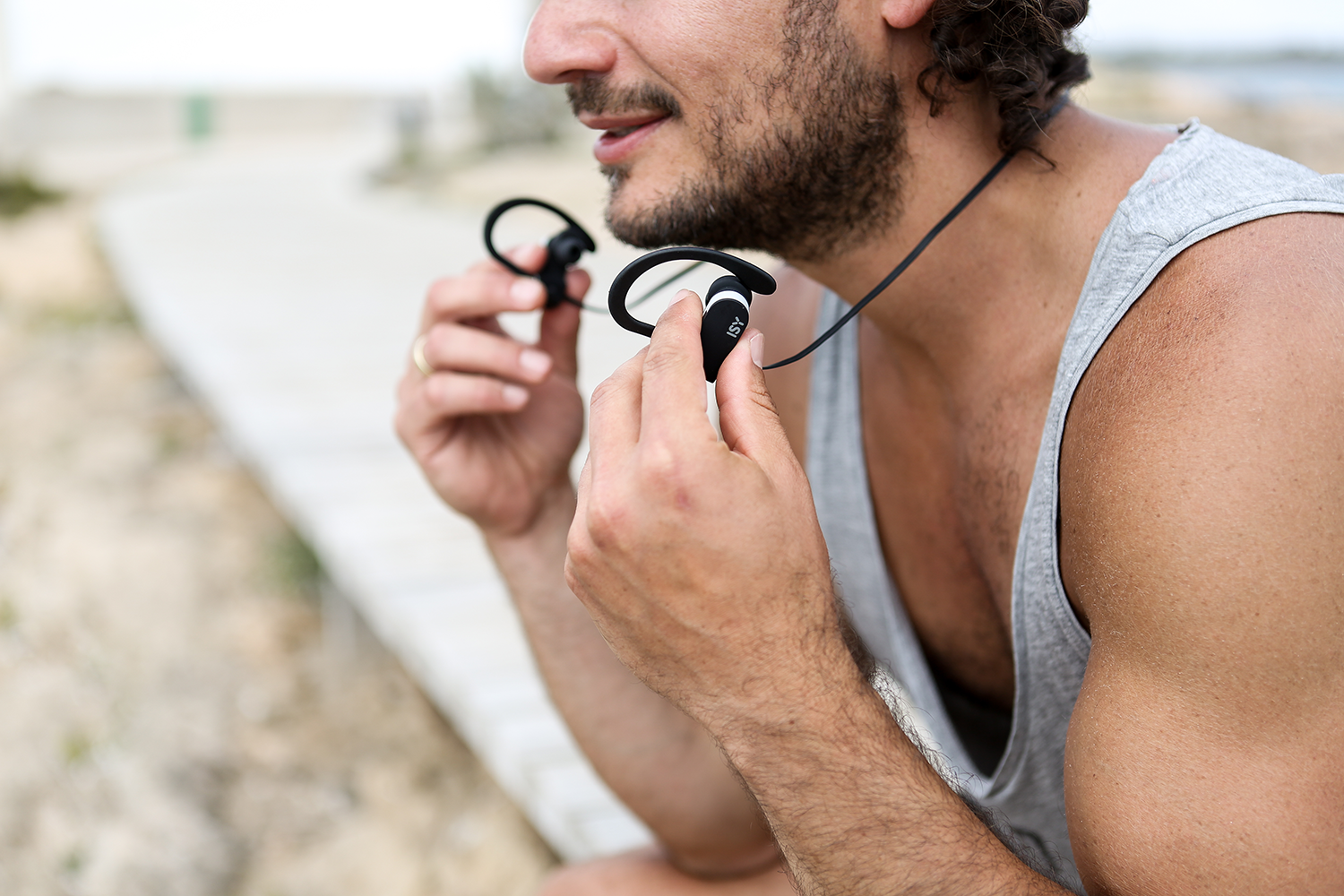 A man holding black earphones, wearing a gray tank top.