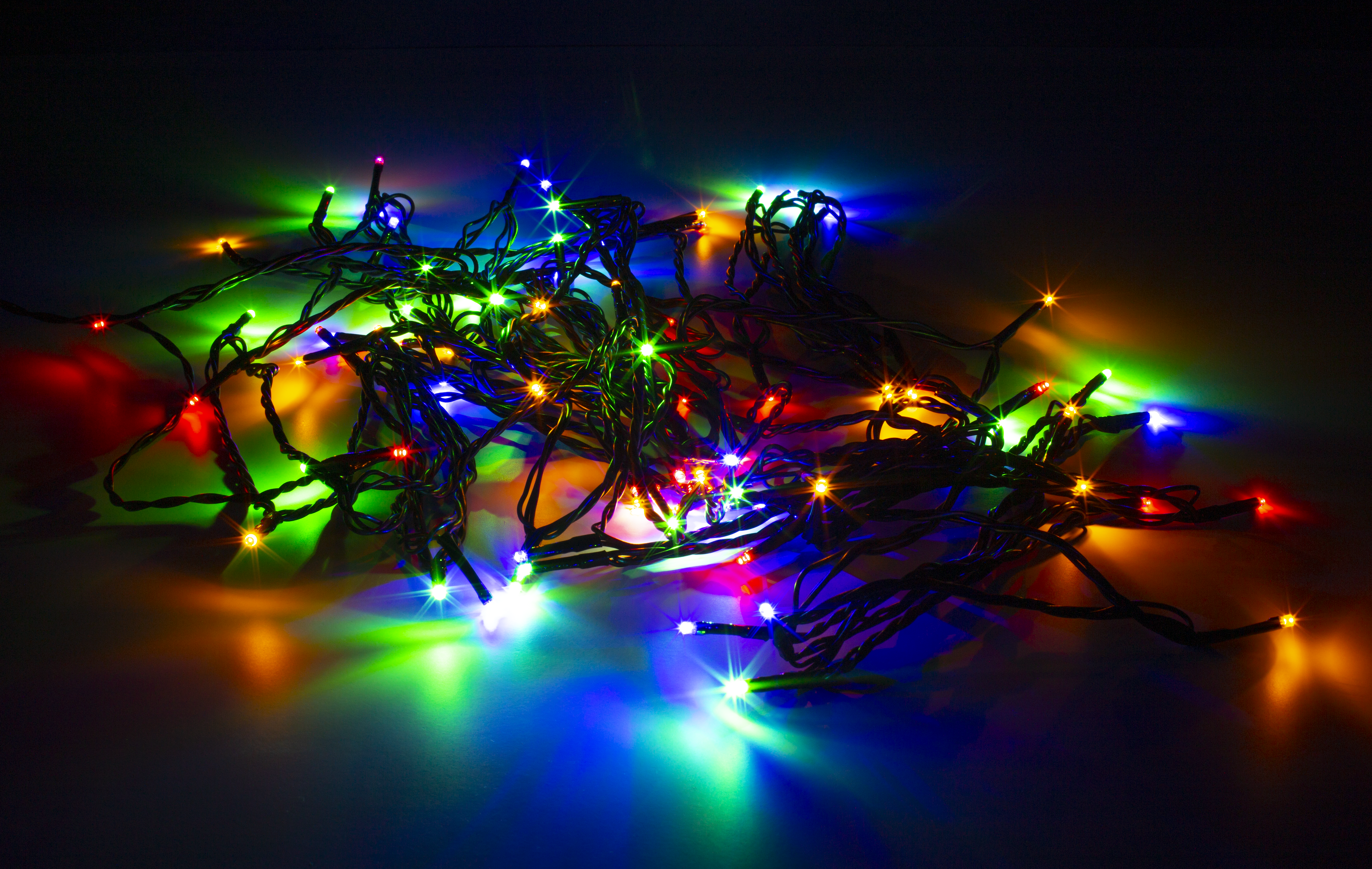 Verwickelte Weihnachtsbeleuchtung in vielen Farben auf dunkler Oberfläche. Grüne, rote und blaue Lichter sind sichtbar.