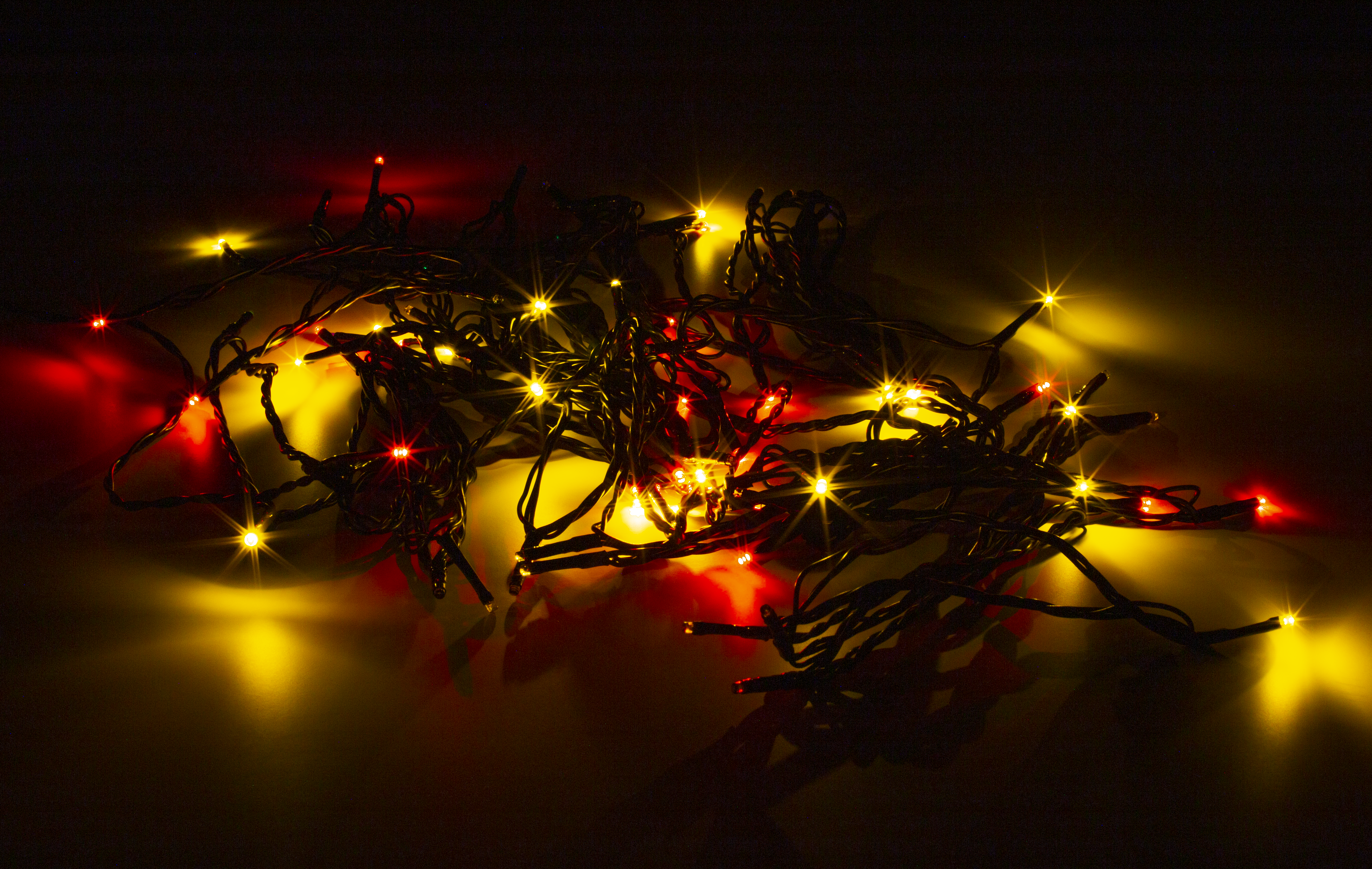 Nahaufnahme von verknoteten Weihnachtslichtern mit roten und gelben Glühbirnen, dunkler Hintergrund.