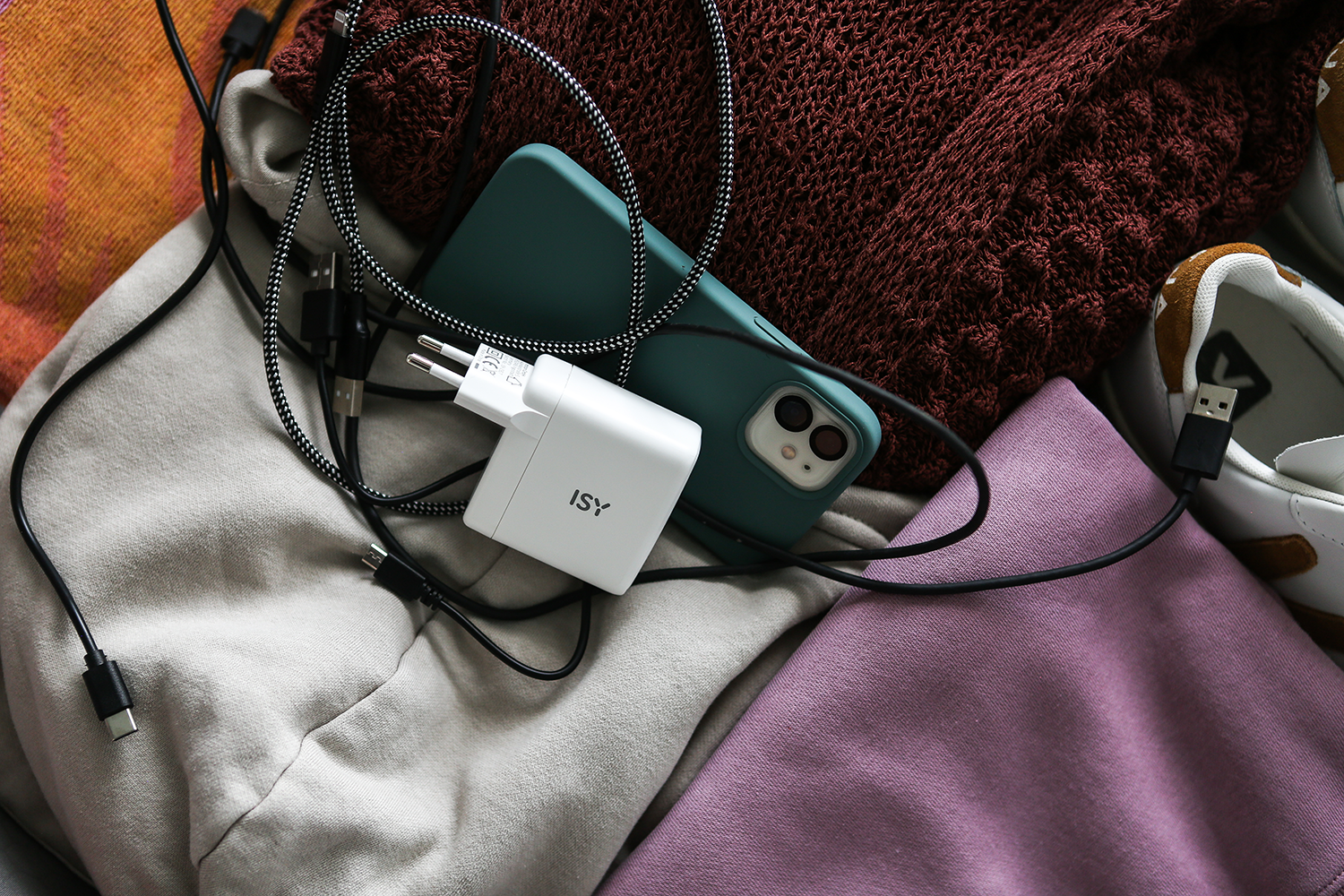 Phone, charger, and cables on fabric. Colors: green phone, white charger, black cables, and various clothes.