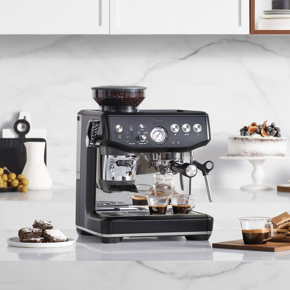 Machine à expresso noire avec un moulin à grains, deux tasses à expresso et une buse vapeur sur un comptoir en marbre.