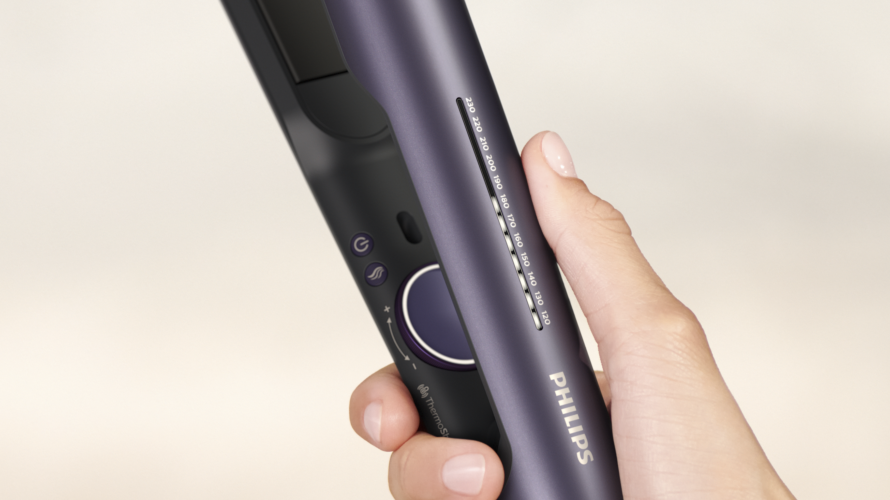 Una mano sostiene una plancha de pelo Philips morada. La plancha tiene ajustes de temperatura y botones de encendido.