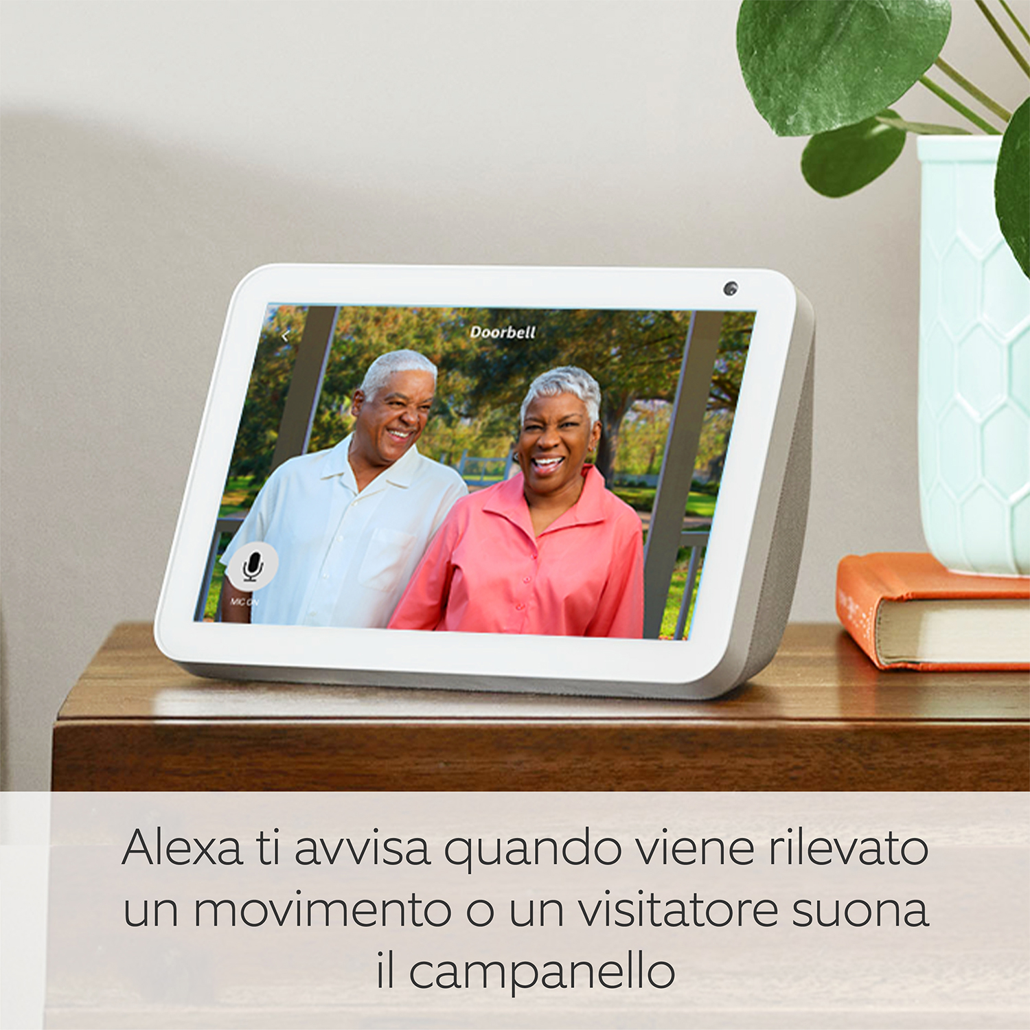 Uno schermo intelligente mostra due persone sorridenti. È su un tavolo con pianta, libro e testo.