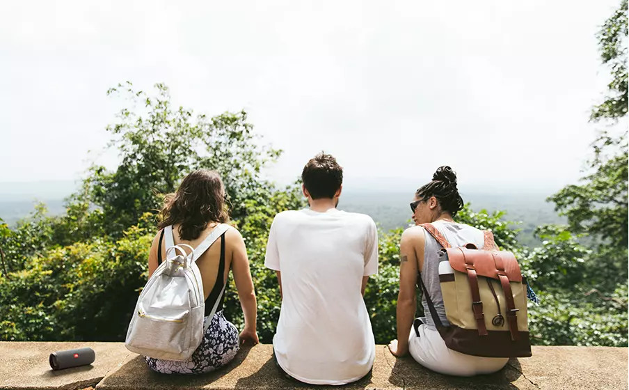 Trois personnes avec des sacs à dos assises sur un mur de pierre surplombant une vue panoramique.