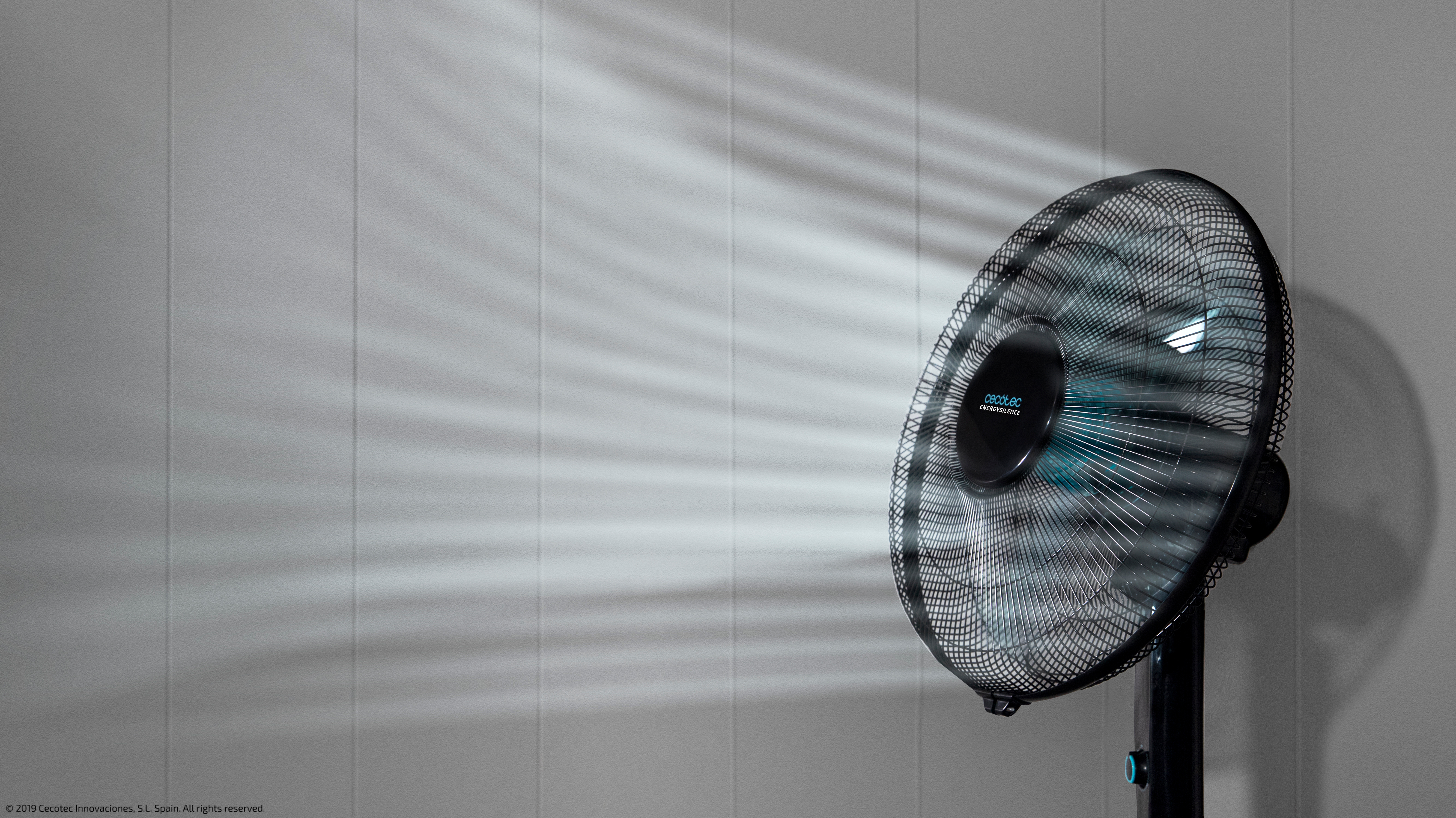 Un ventilador negro soplando aire. La luz del ventilador crea un patrón en la pared.
