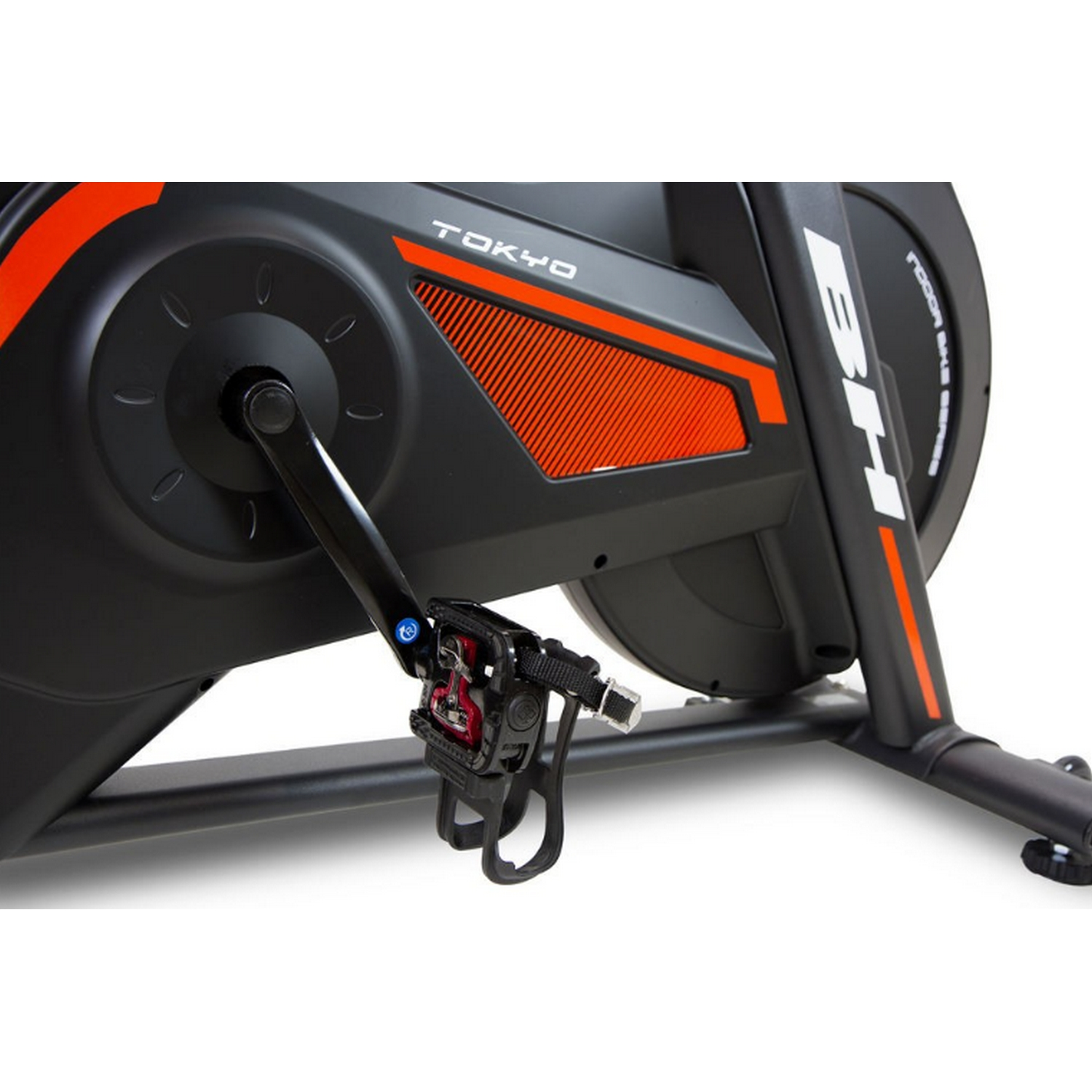 Bicicleta estática con detalles en negro y naranja, primer plano. Fondo blanco.