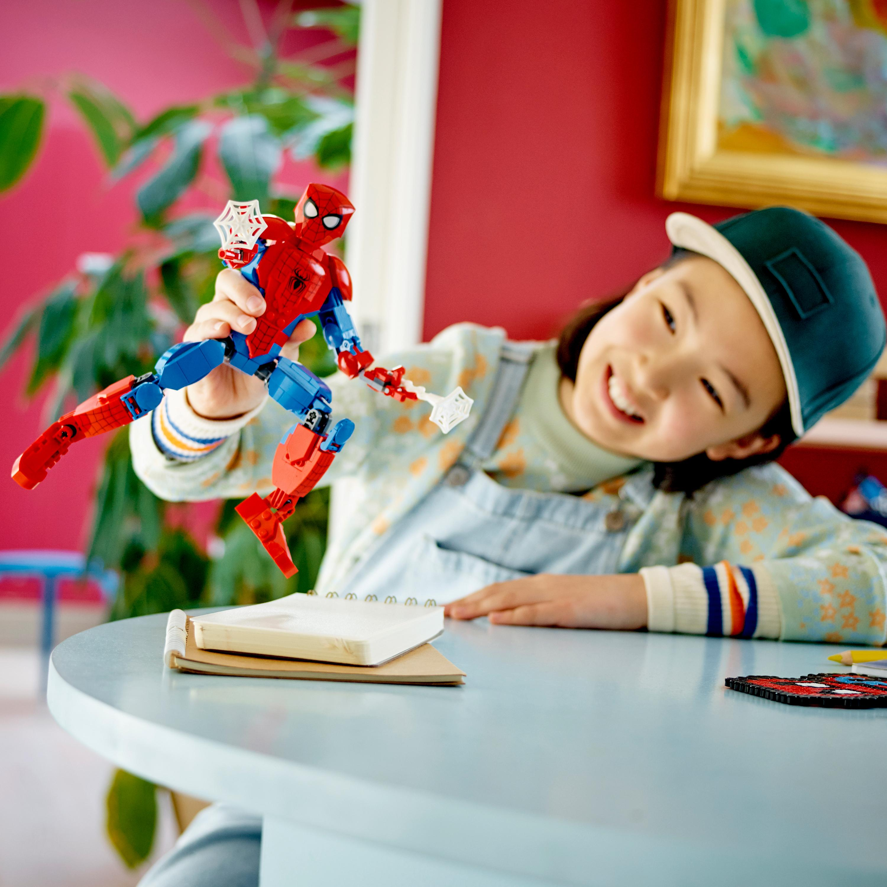 Ein Mädchen spielt mit einer Spiderman-Lego-Figur. Sie lächelt und der Hintergrund hat eine rote Wand.
