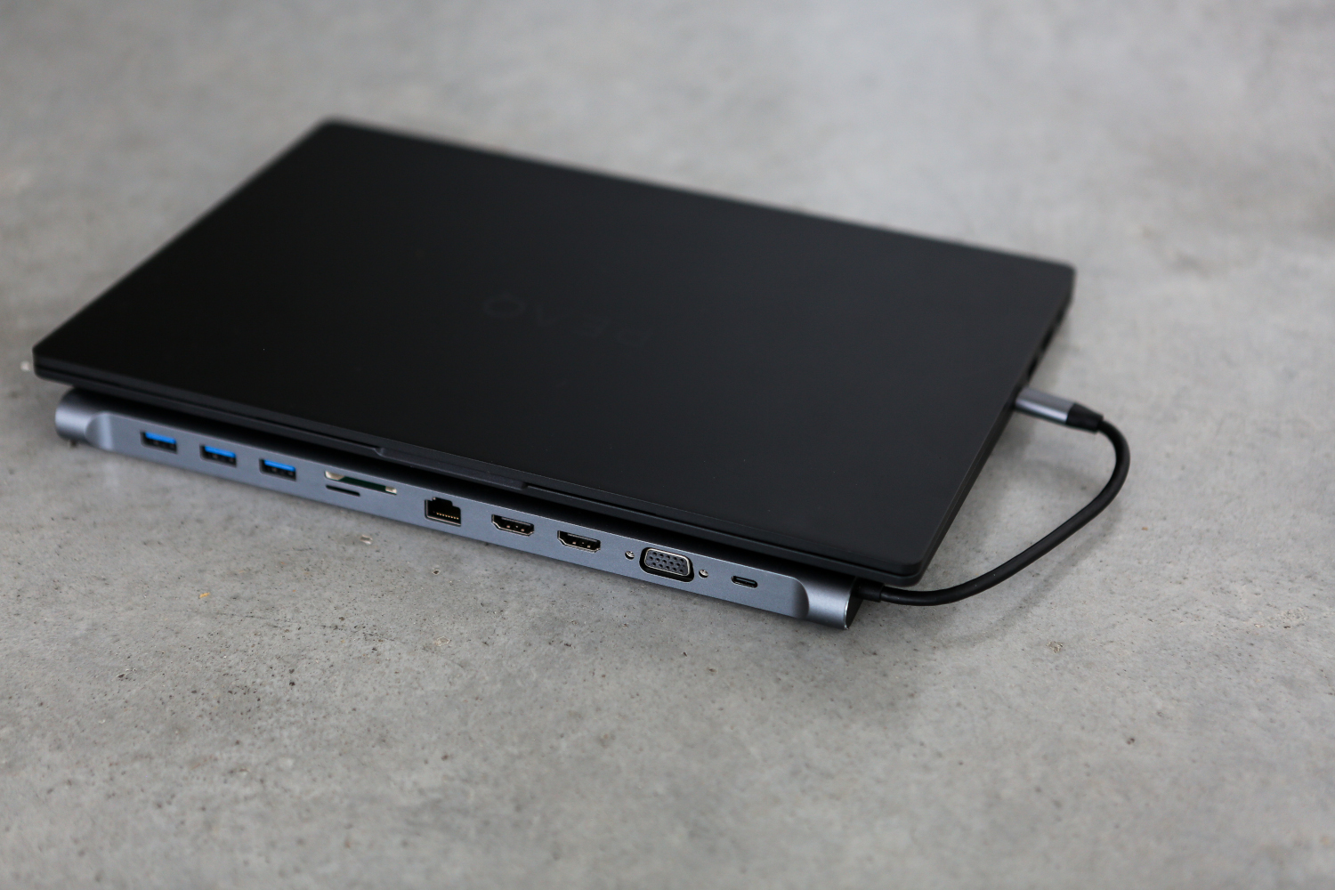 Un ordinateur portable connecté à un hub. L'ordinateur portable est noir, et le hub est argenté, sur une surface grise.