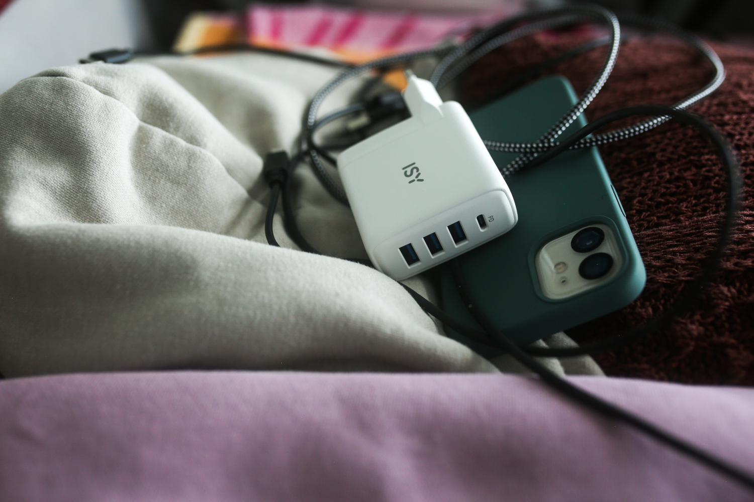 Witte oplader, groene telefoon en zwarte kabel op een beige en roze oppervlak.