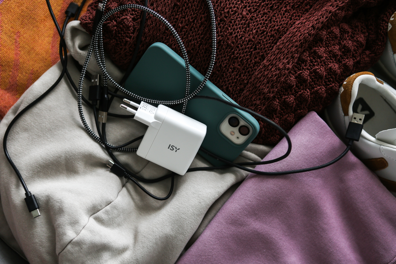 Een oplader, telefoon en kabels op een bed.