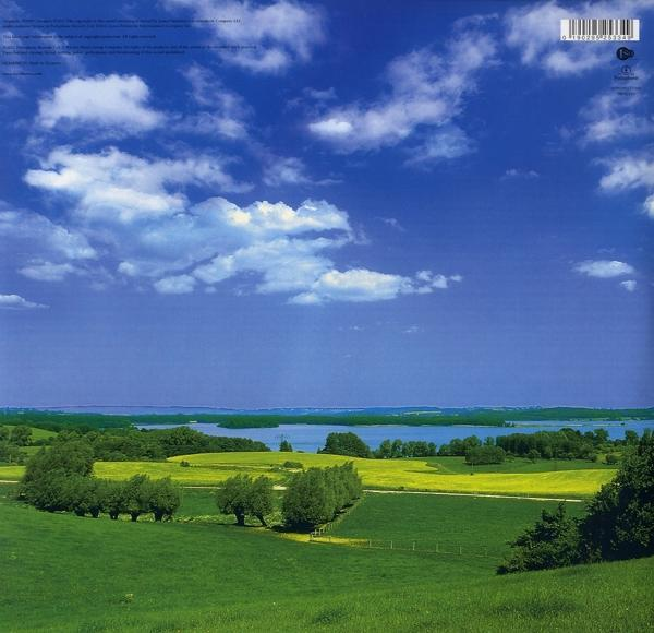 Landschaft mit blauem Himmel und Wolken. Grüne Felder und Bäume, See im Hintergrund.