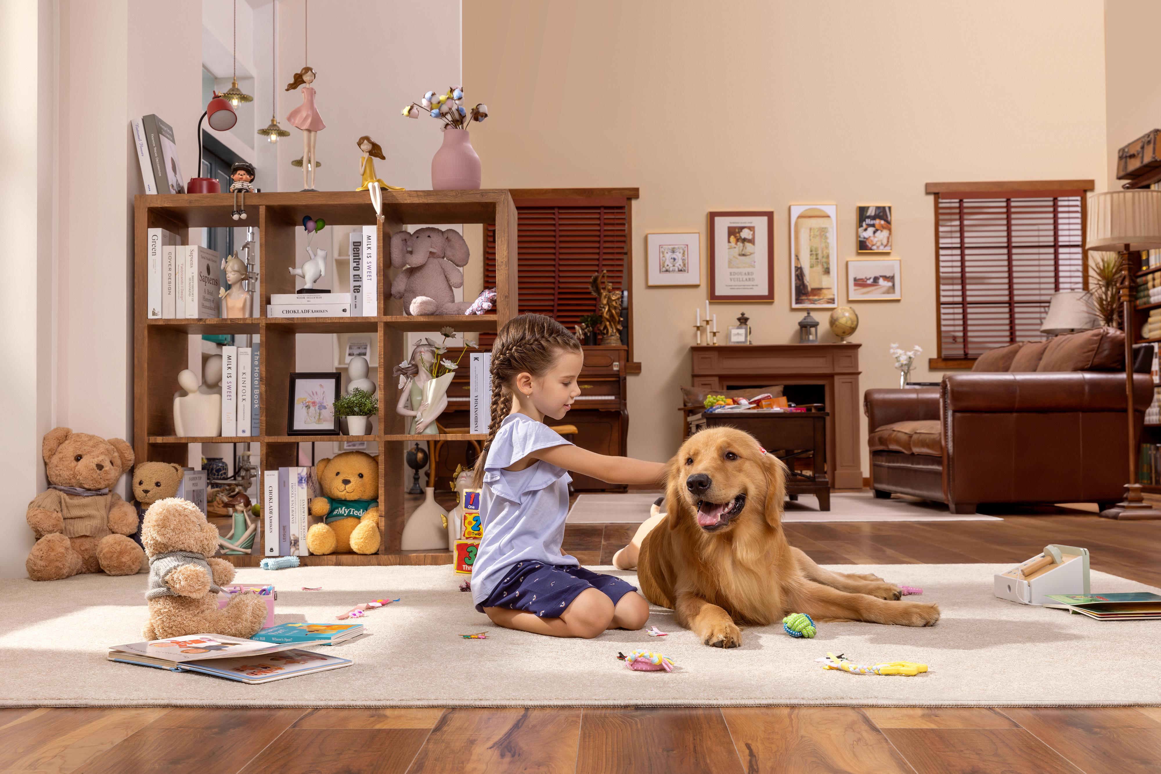 Ein kleines Mädchen streichelt einen Golden Retriever-Hund in einem Wohnzimmer mit Bücherregalen und Spielzeug.