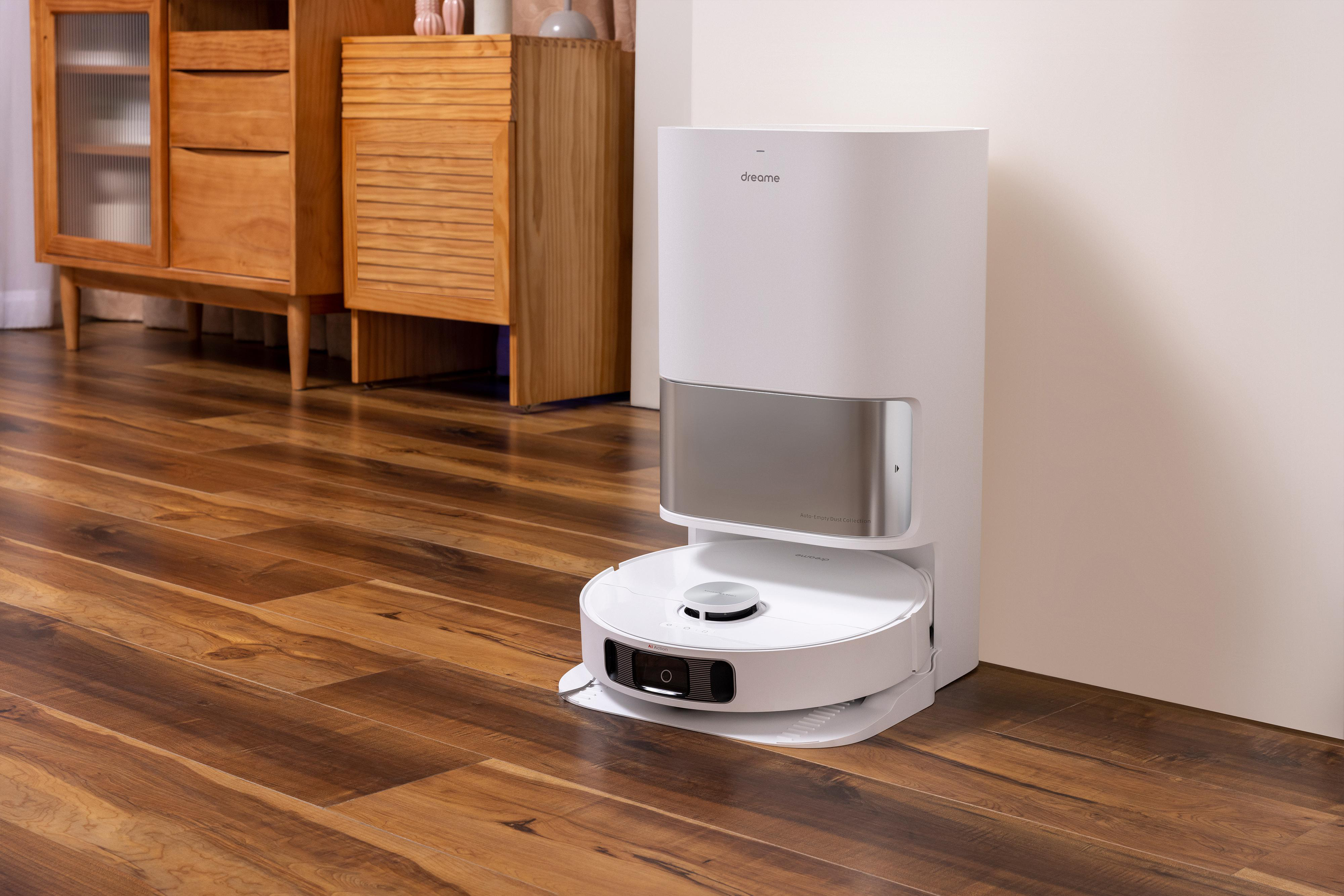 Weißer Roboter-Staubsauger mit Dockingstation auf Hartholzboden. Holzmöbel im Hintergrund.