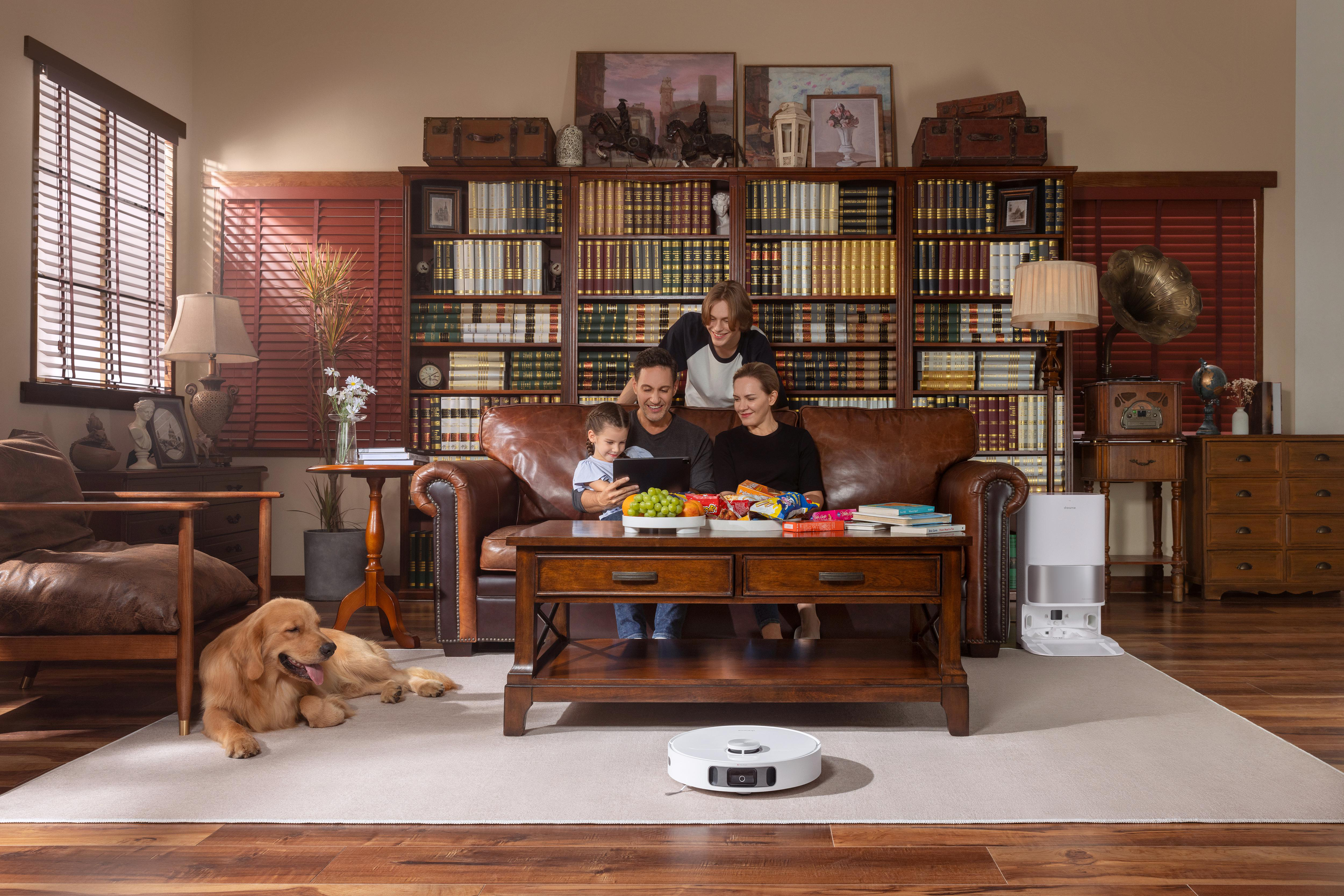 Familie auf Couch, Hund und Roboter-Staubsauger in einem Wohnzimmer mit Bücherregal.