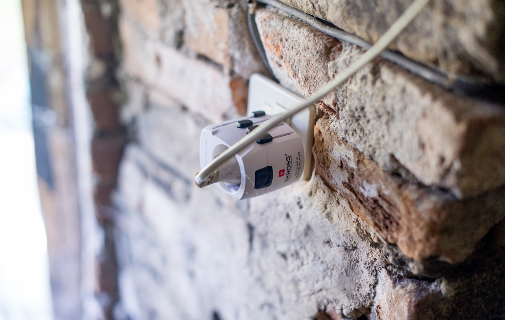 Un adattatore elettrico collegato a una parete. Il muro è di mattoni.