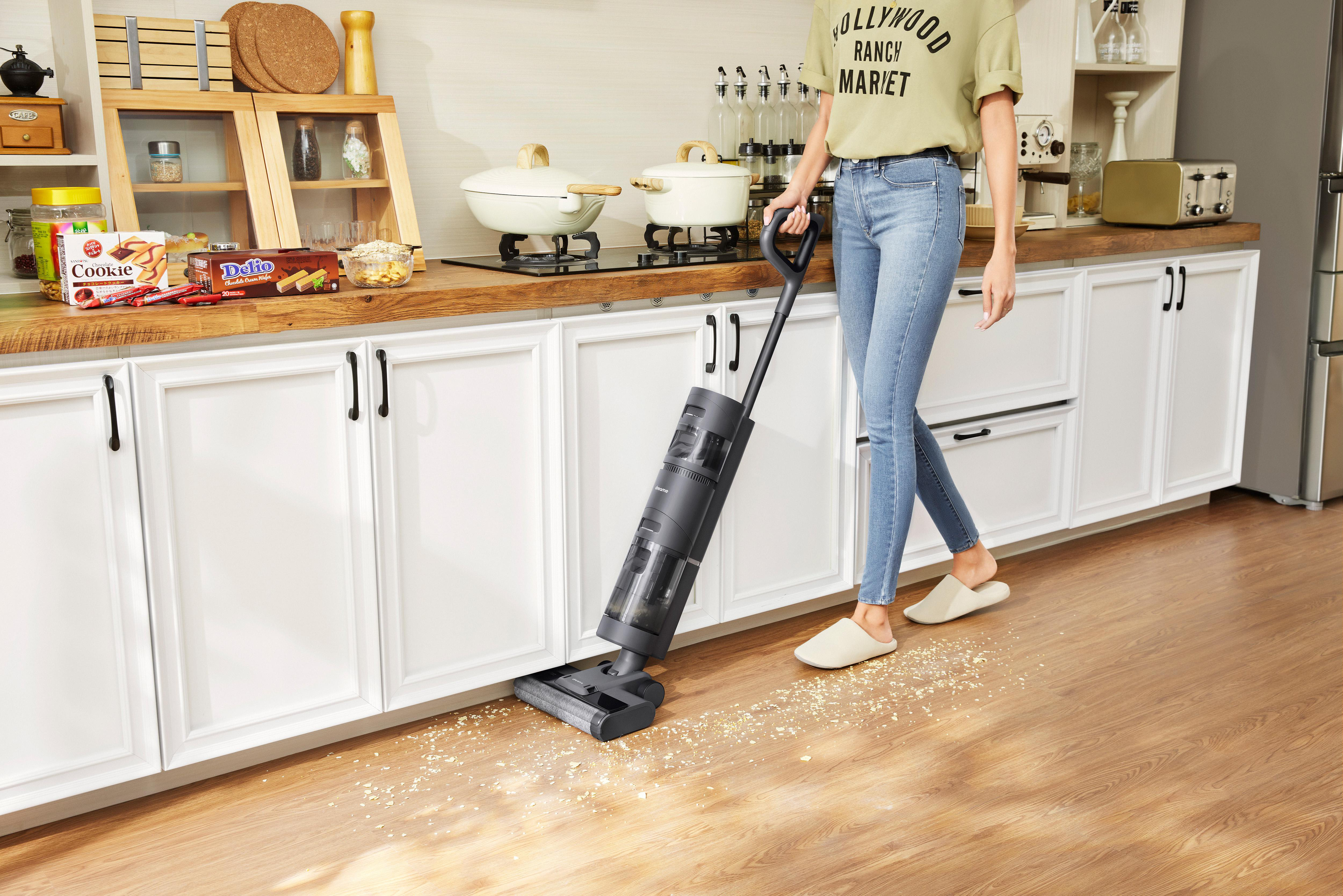 Frau saugt Küchenboden mit einem schwarz-grauen Staubsauger.