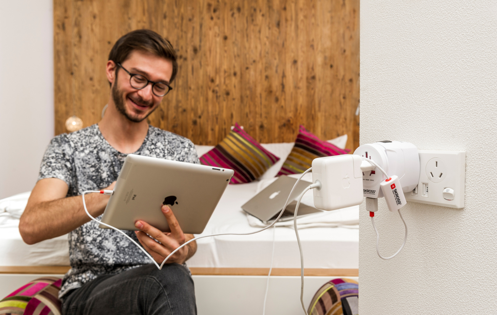 Uomo che carica iPad e laptop con più spine e adattatori.