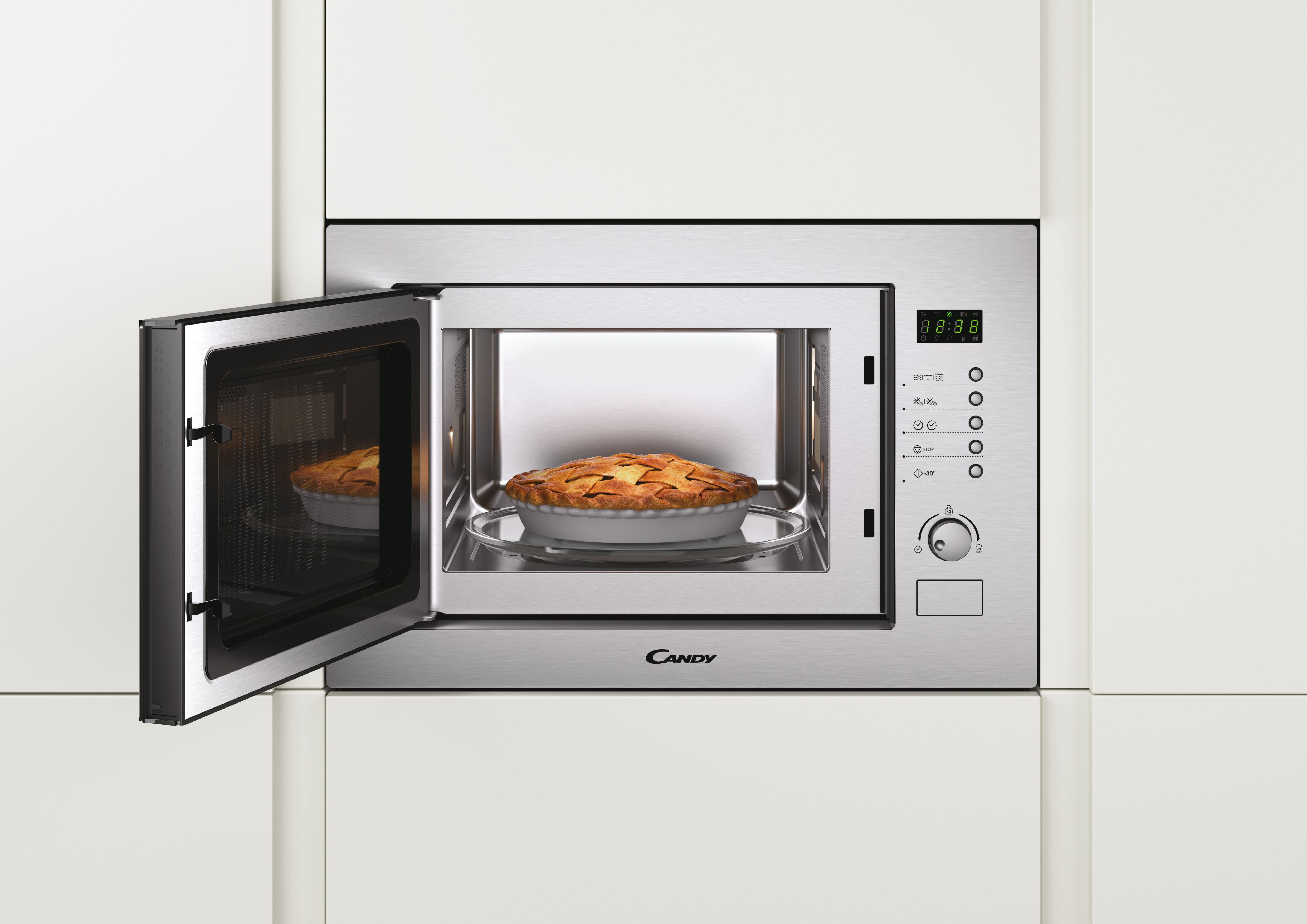 Un horno microondas Candy abierto con un pastel dentro, en una pared blanca de cocina.