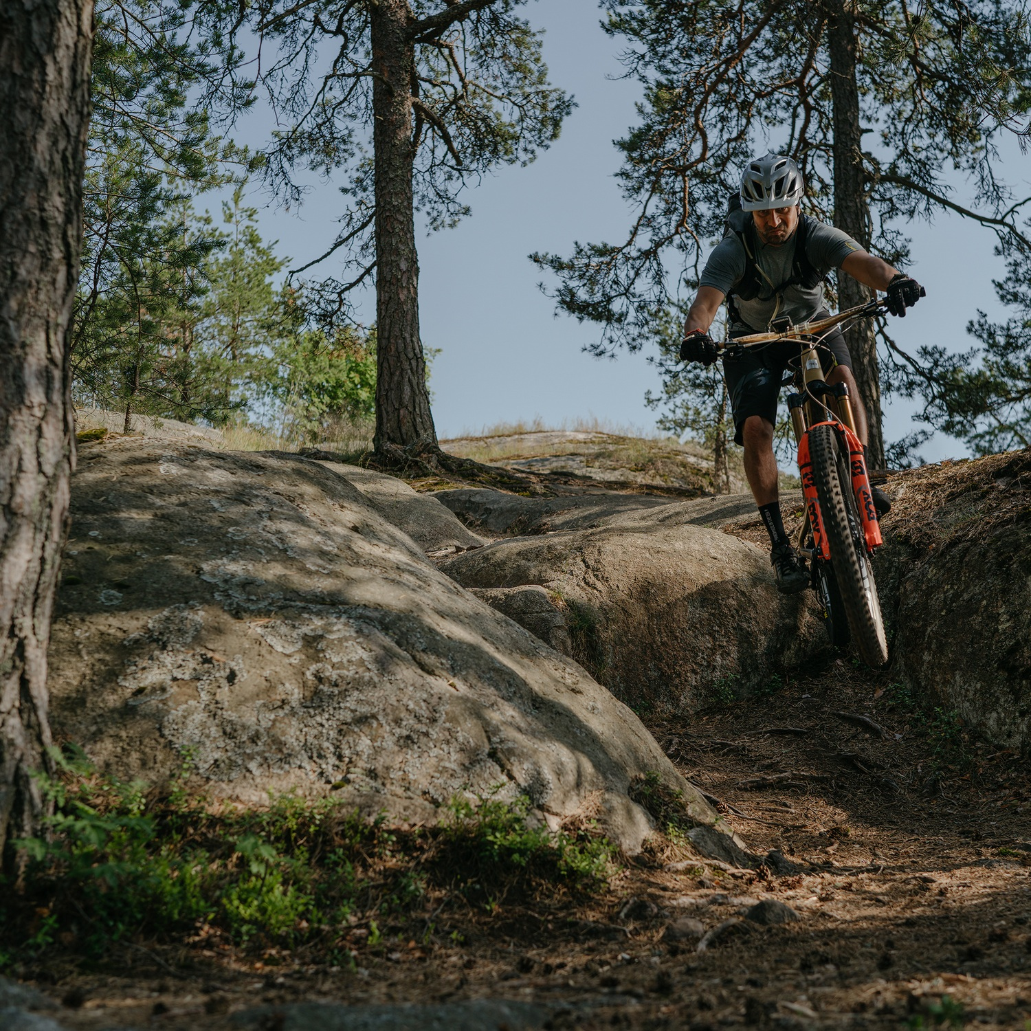 Un hombre en bicicleta de montaña monta sobre rocas en un entorno forestal.