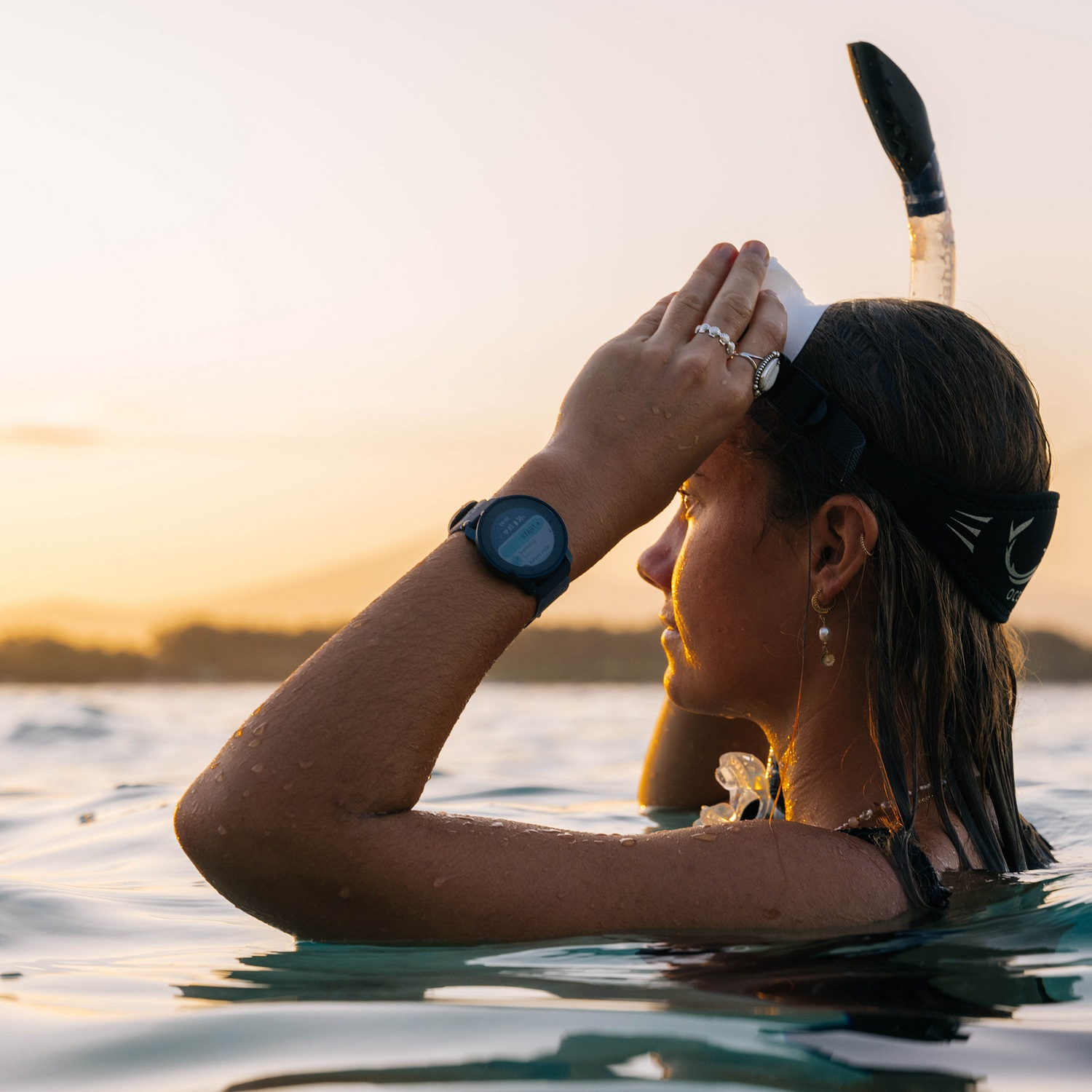 Mujer en el agua con máscara de snorkel, viendo el atardecer.
