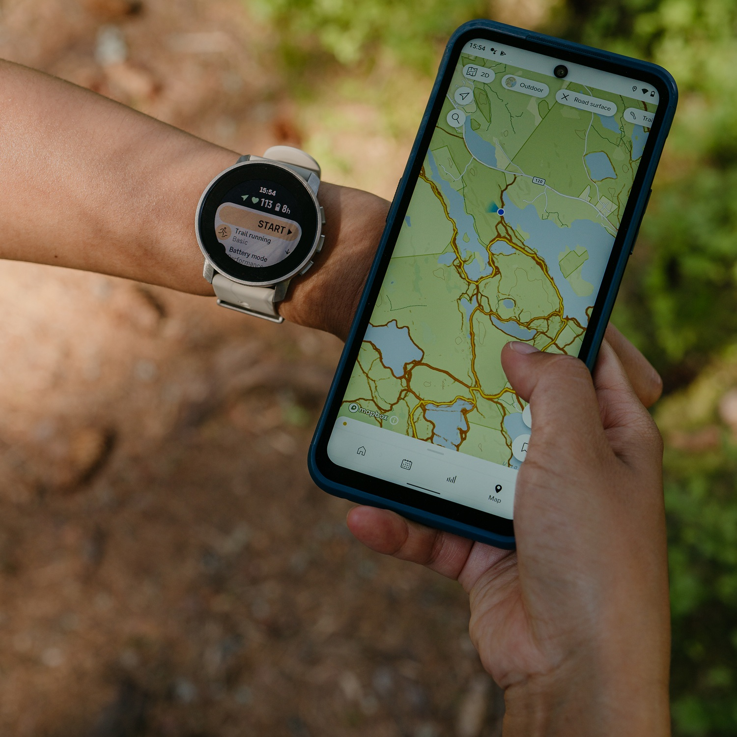 Brazo con smartwatch y smartphone. La esfera del reloj muestra datos de actividad, el teléfono un mapa.