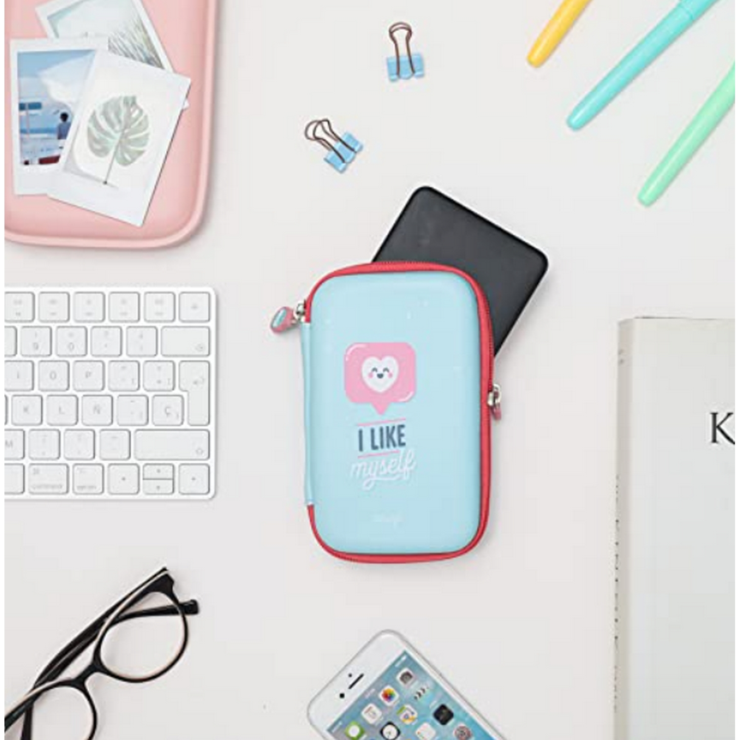 Configuración de escritorio con una bolsa azul, teclado, gafas, teléfono y otros útiles de oficina.