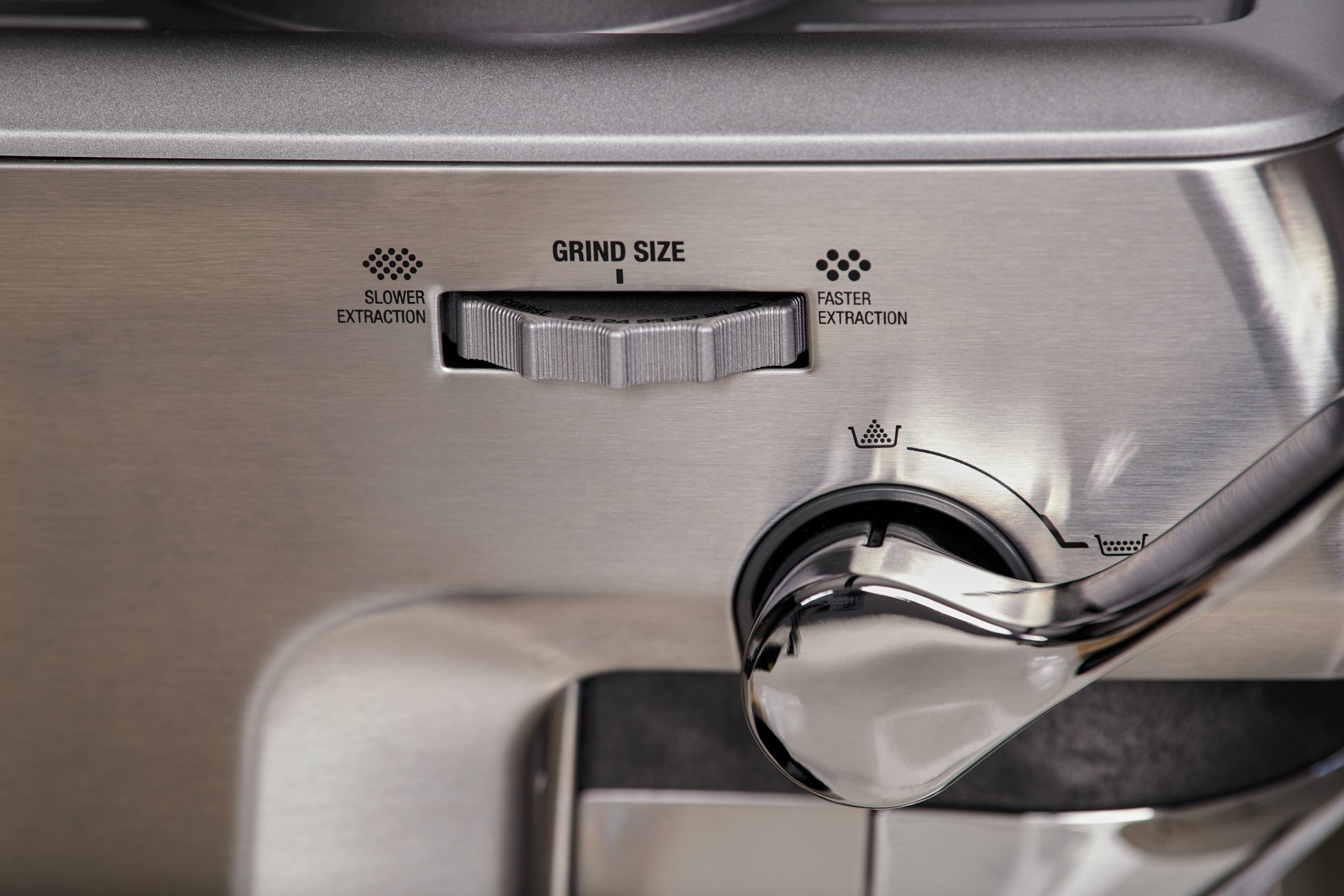Nahaufnahme einer Kaffeemaschine. Es zeigt den Mahlgradregler mit dem Text 'Langsamere Extraktion' und 'Schnellere Extraktion'.