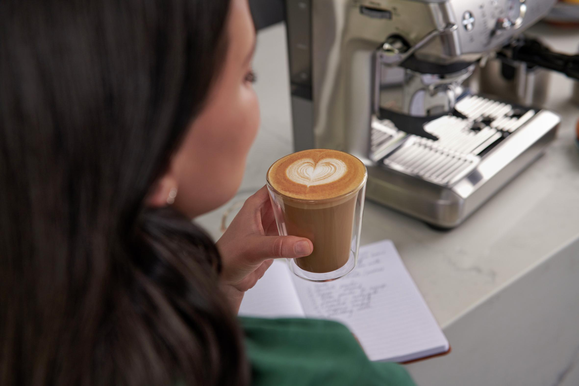Person hält Kaffee mit Latte Art und Notizbuch.