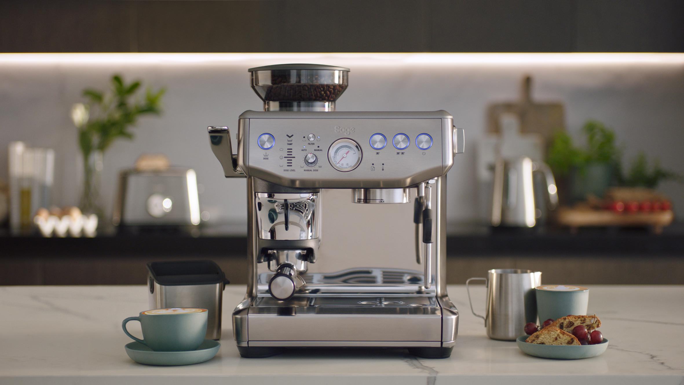 Eine moderne silberne Kaffeemaschine mit einer Tasse Kaffee und Gebäck auf dem Tisch.