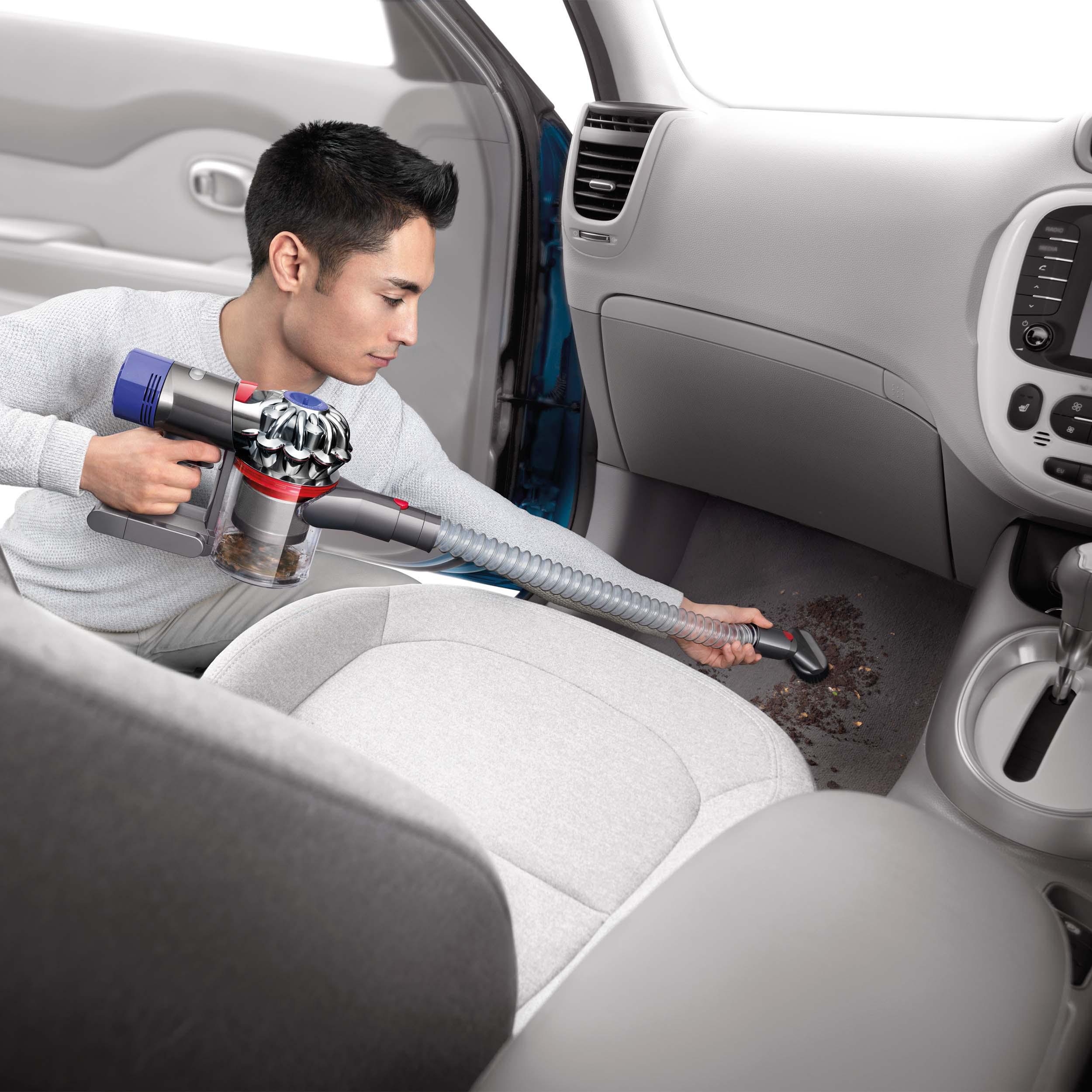 Ein Mann, der das Innere eines Autos saugt. Der Staubsauger ist ein Handmodell von Dyson.