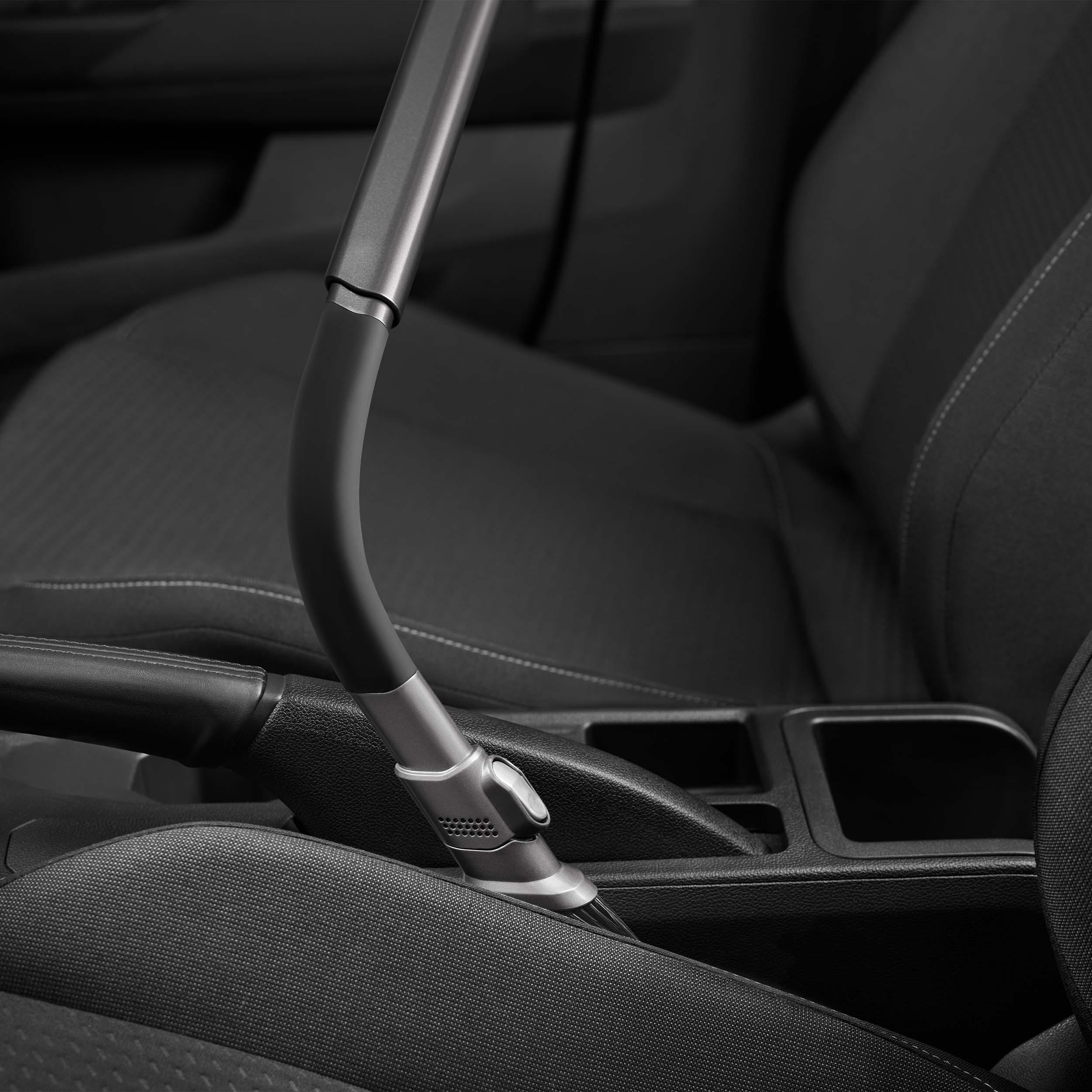 Ein Staubsaugeraufsatz in einem Autoinnenraum, zwischen Sitzen und Konsole. Dunkelgraue und schwarze Farben.
