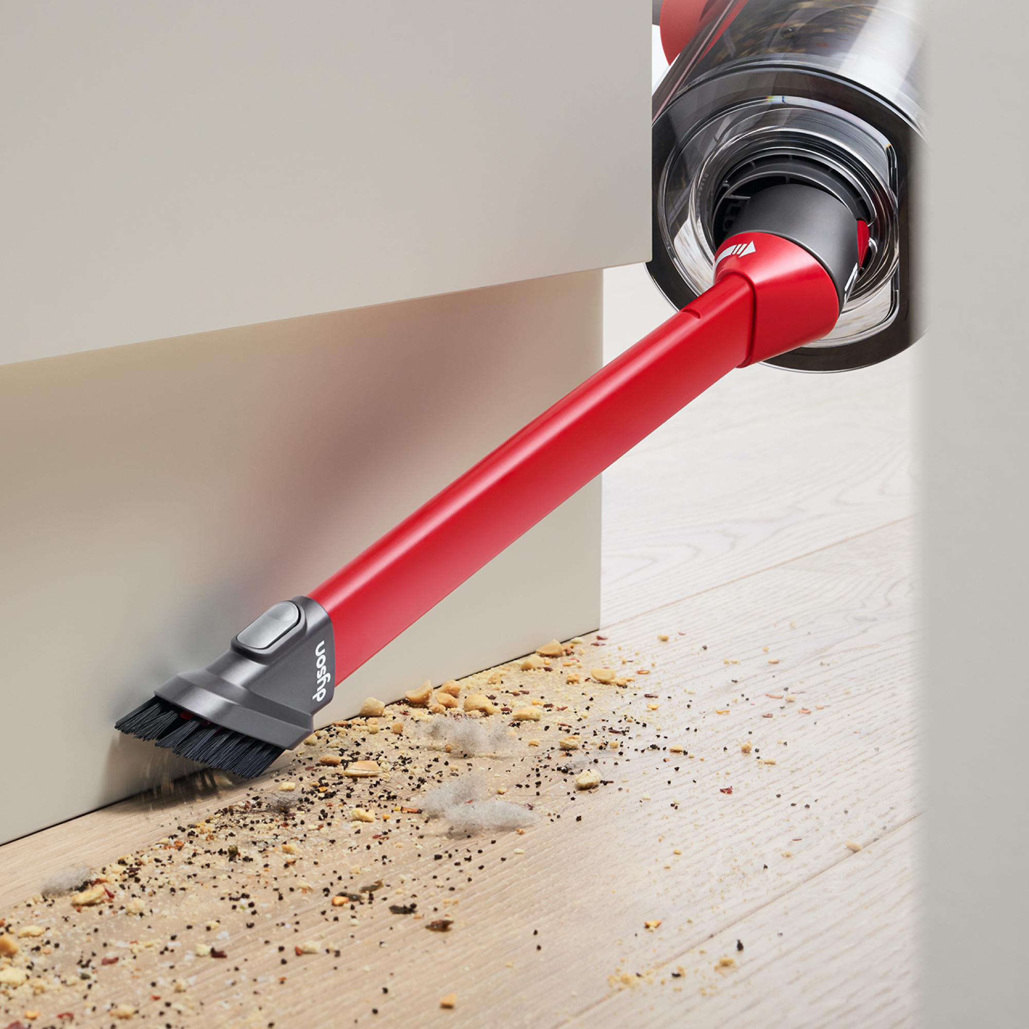 Ein roter Staubsaugeraufsatz, der Schmutz von einem Holzboden in der Nähe einer Wand reinigt.