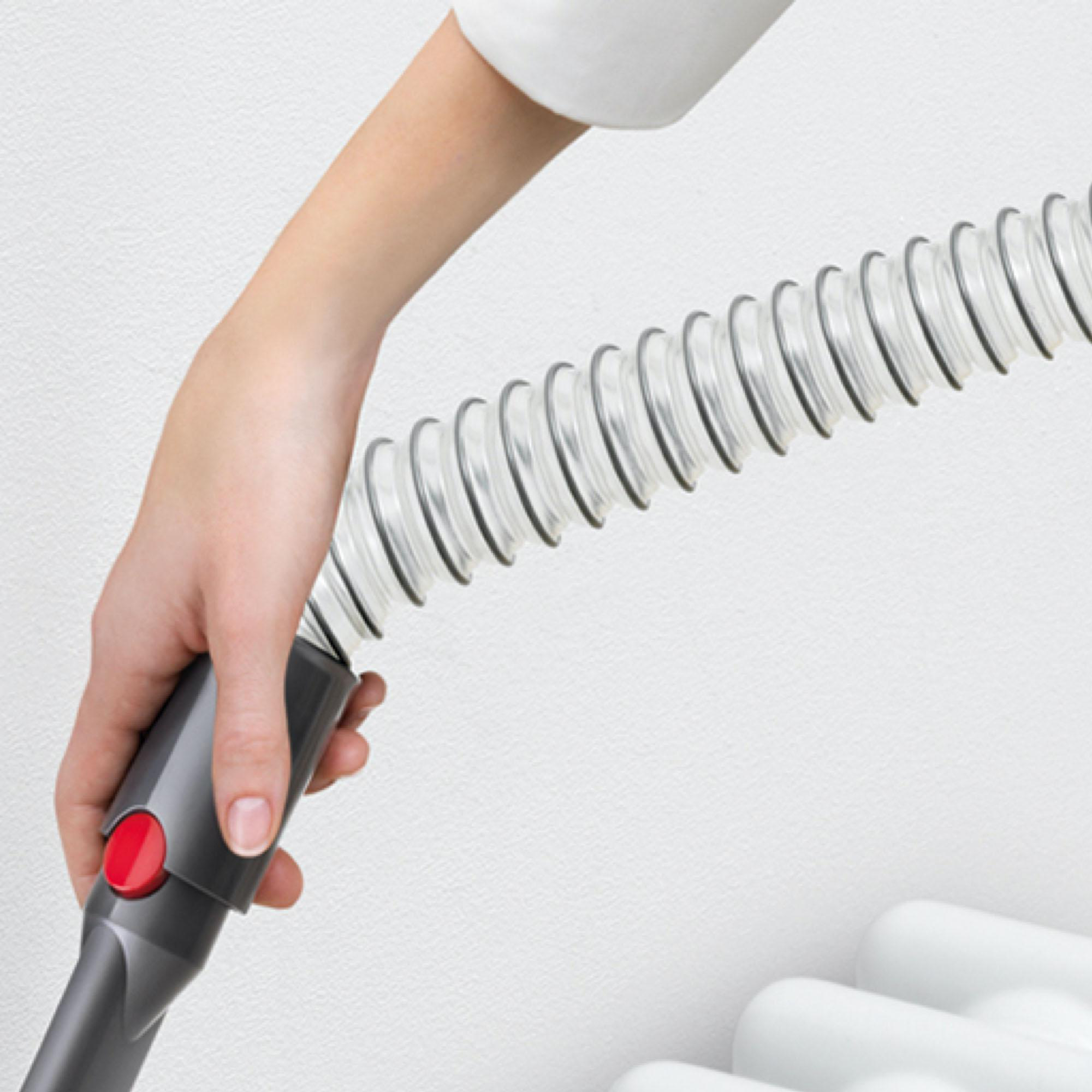 Eine Hand hält einen Staubsaugerschlauch in der Nähe einer weißen Wand und eines Heizkörpers.