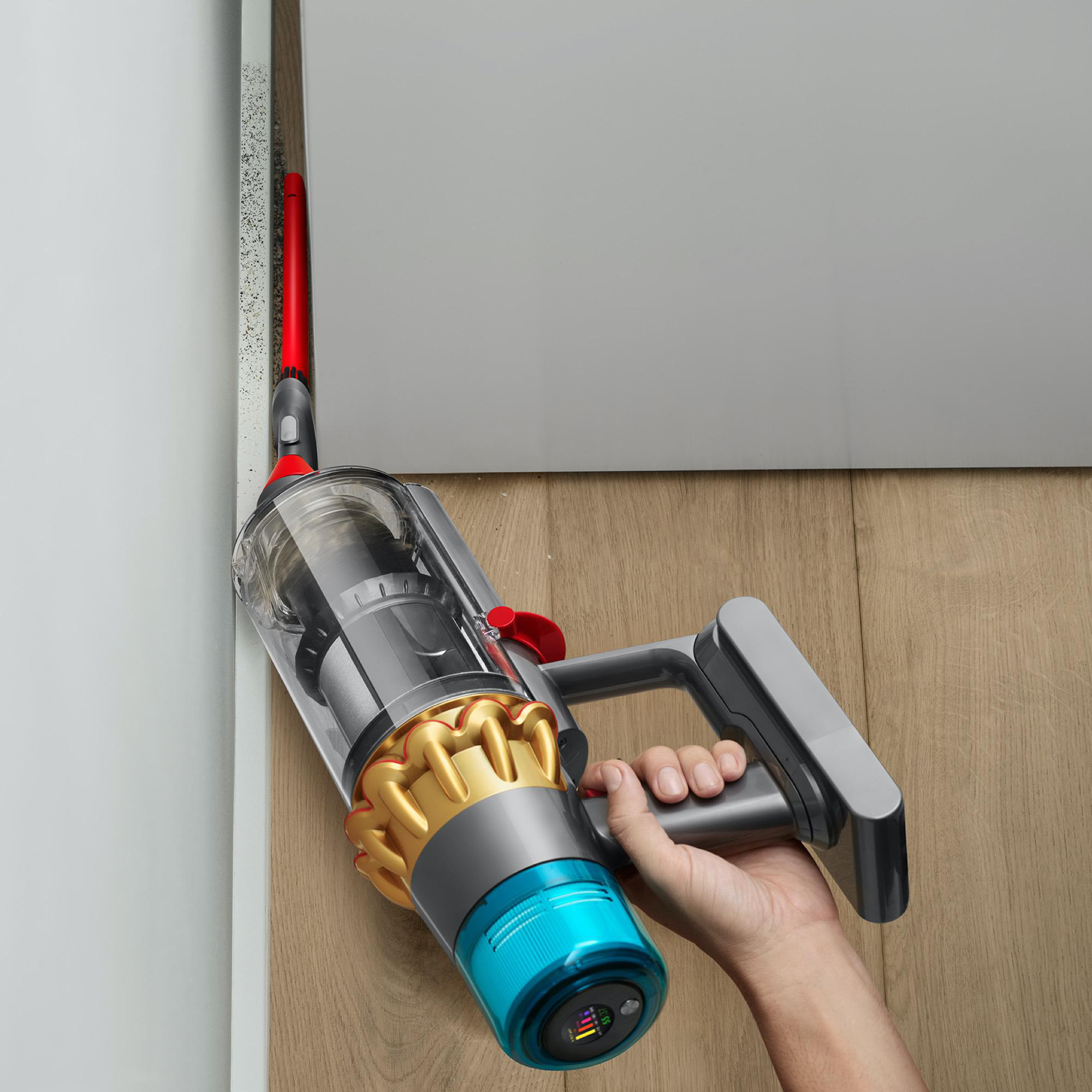 Eine Person hält einen Dyson-Staubsauger und reinigt eine Wandkante. Der Staubsauger ist in Betrieb.